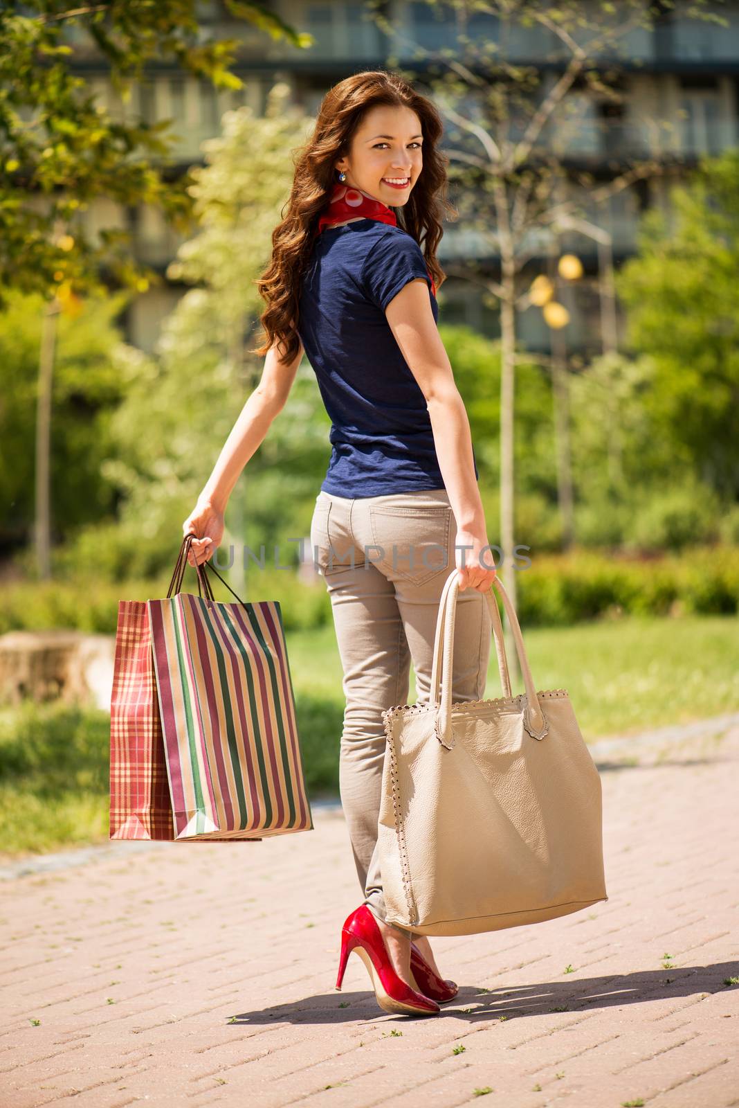 Beautiful young woman walking in the park and holding shopping bags.