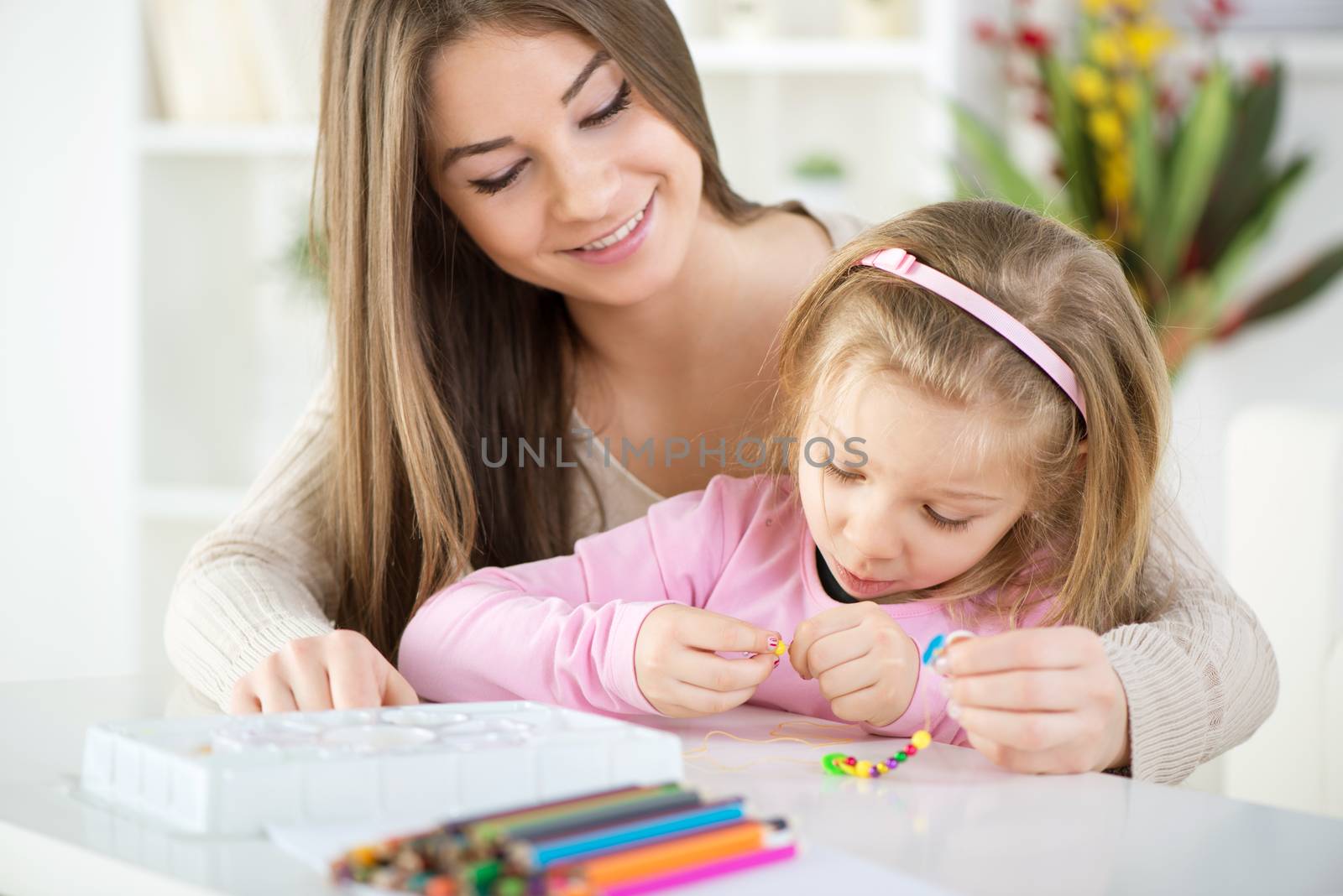 Mother and daughter playing at home. They Making bead bracelets.