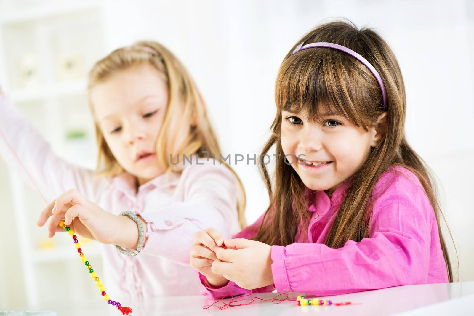 Two cute little girls Making bead jewelry at home 