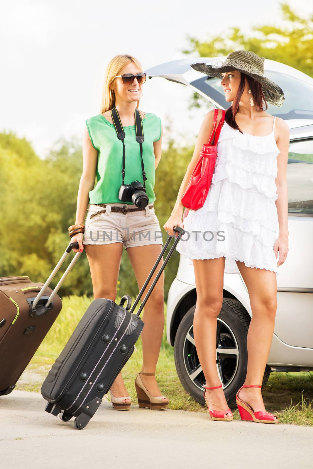 Happy young women with luggage standing by the car. They pack up their bags and going on holiday.