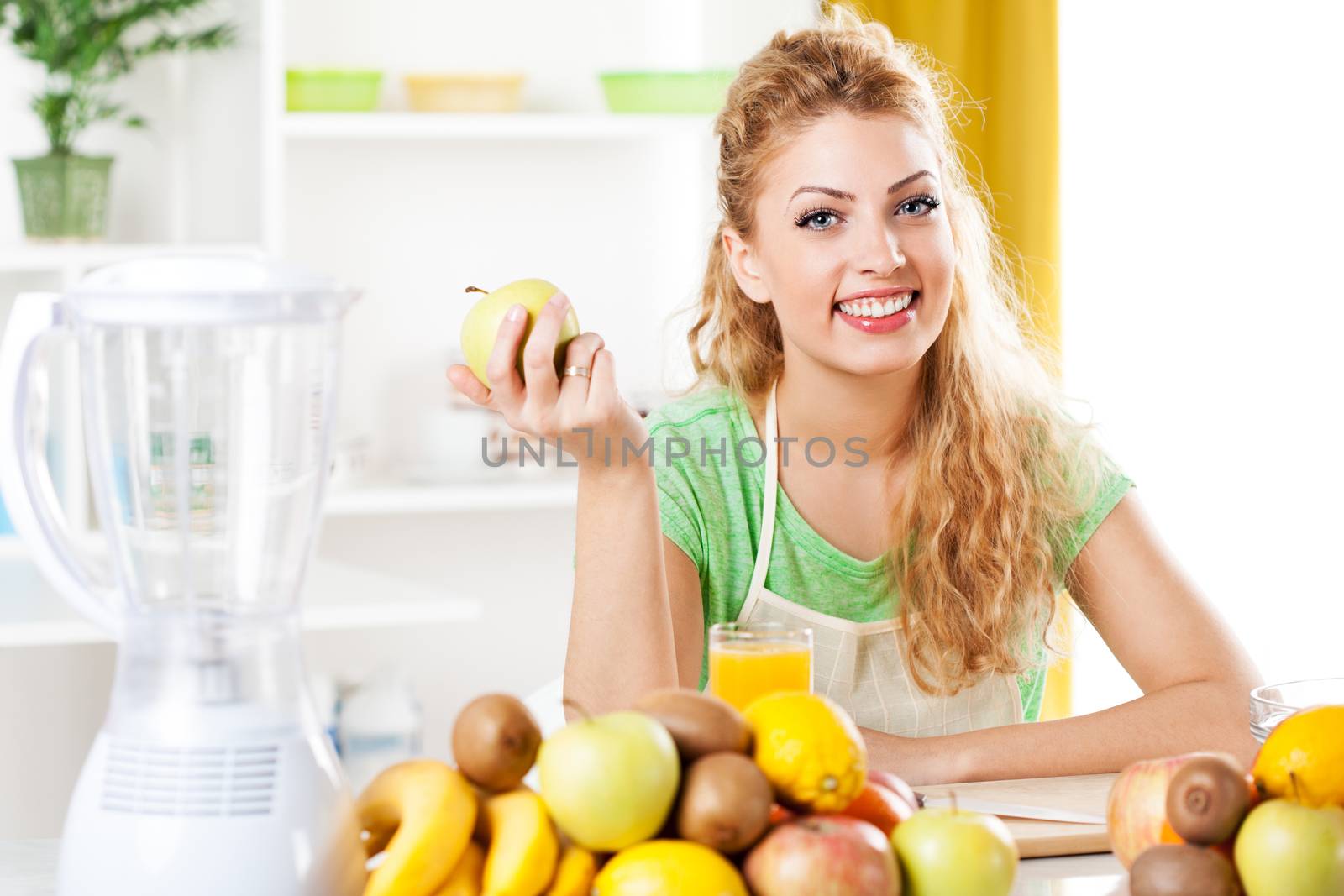 Beautiful young woman in a kitchen, holding an apple. Looking at camera.