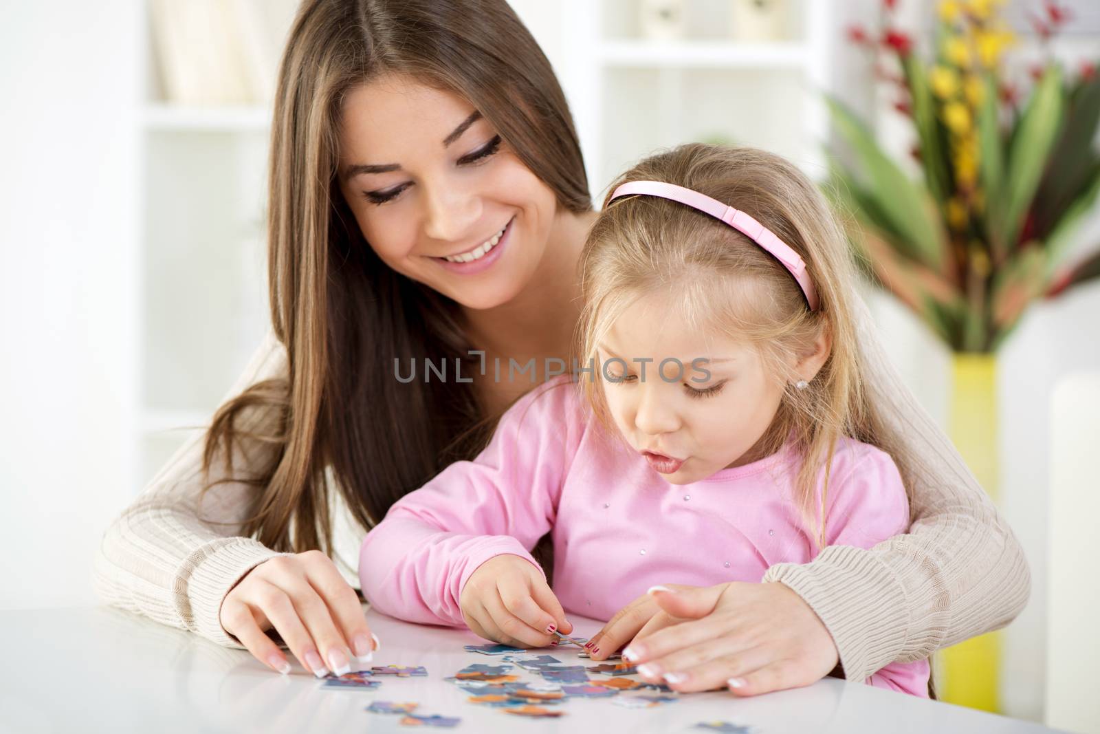 Mother and daughter playing at home. They assembling Jigsaw Puzzle.