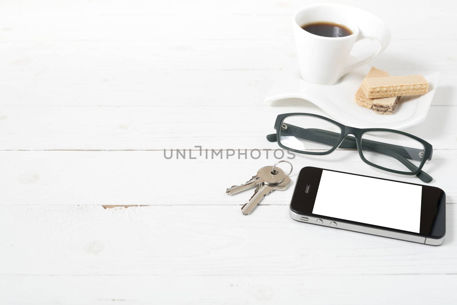 coffee cup with wafer,phone,key,eyeglasses on white wood background