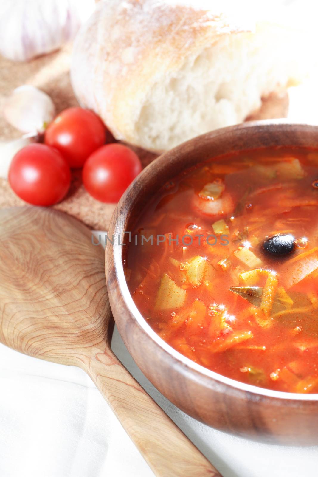 Nice wooden bowl with vegetable soup near bread and tomatoes