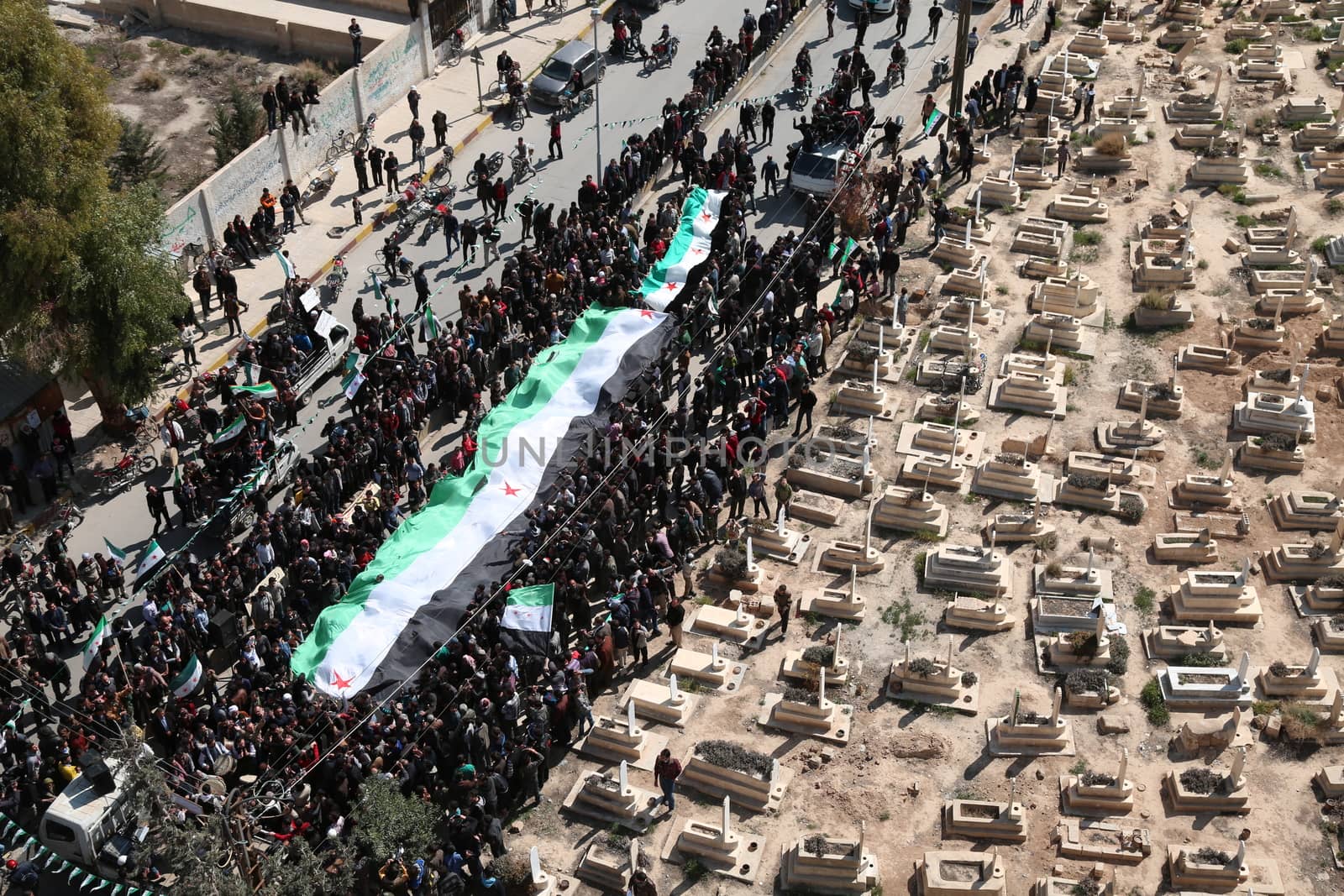 SYRIA, Saqba: Protesters hold a giant pre-Baath Syrian flag, adopted during the uprising in 2011, and placards during an anti-regime demonstration in the rebel-held town of Saqba, on the outskirts of the Syrian capital Damascus, on March 18, 2016. Syria's war is entering its sixth year with a glimmer of hope that a landmark ceasefire and a push for peace could help resolve a conflict that has sent hundreds of thousands fleeing to Europe. The conflict began with anti-regime protests in mid-March 2011 and spiralled into a bloody war after a harsh government crackdown on demonstrators.