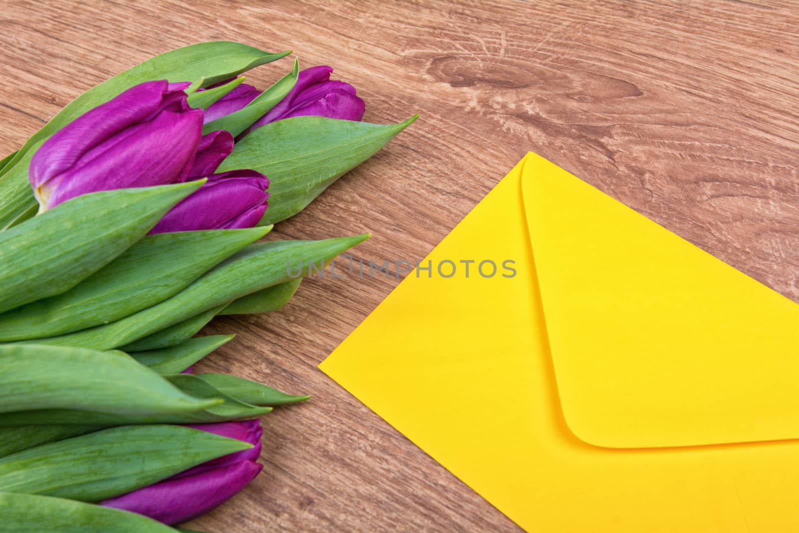 Yellow envelope with purple tulips on a wooden background