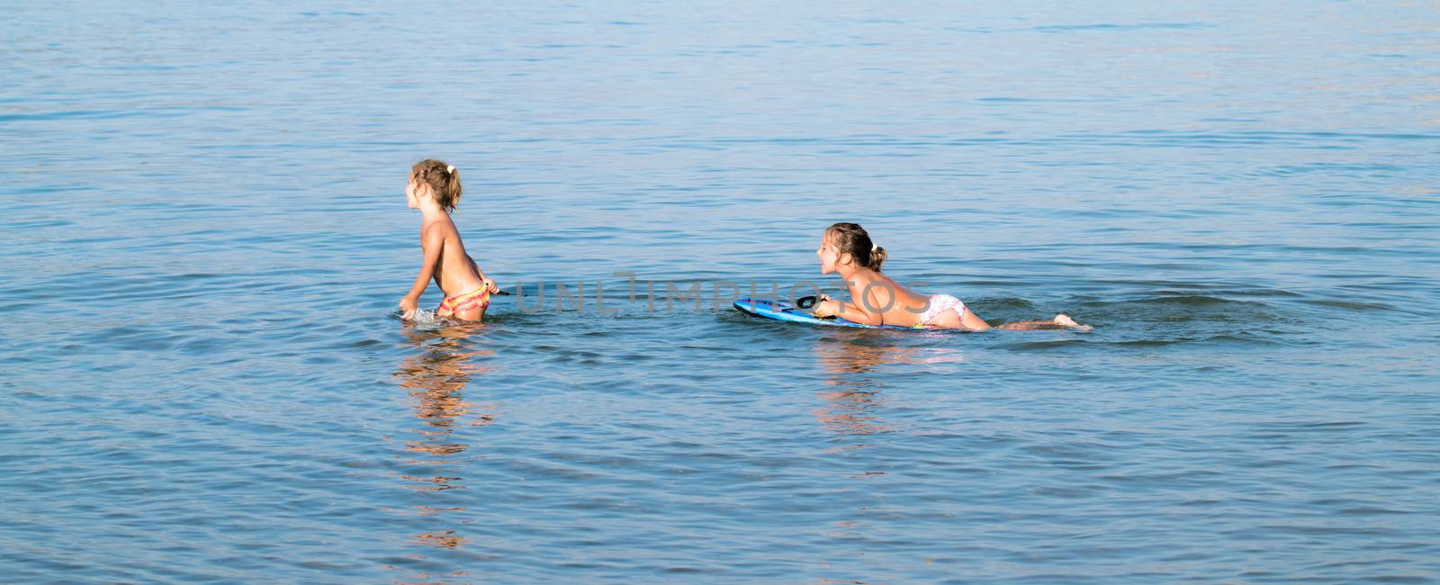 Two little girls playing in the sea with a floating board.