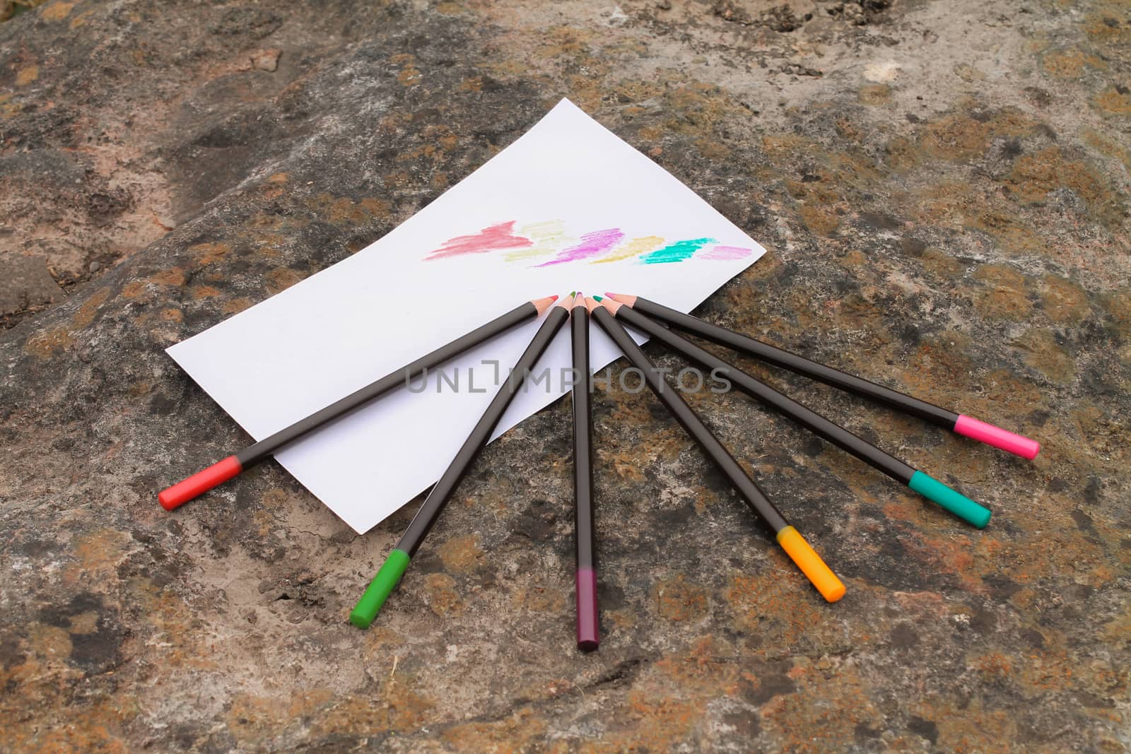 Watercolour pencils, of various colours, arranged on a rock.