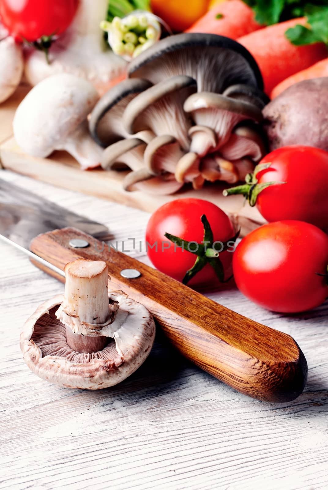 Kitchen knife,mushrooms of two varieties,the tomatoes on light wooden background