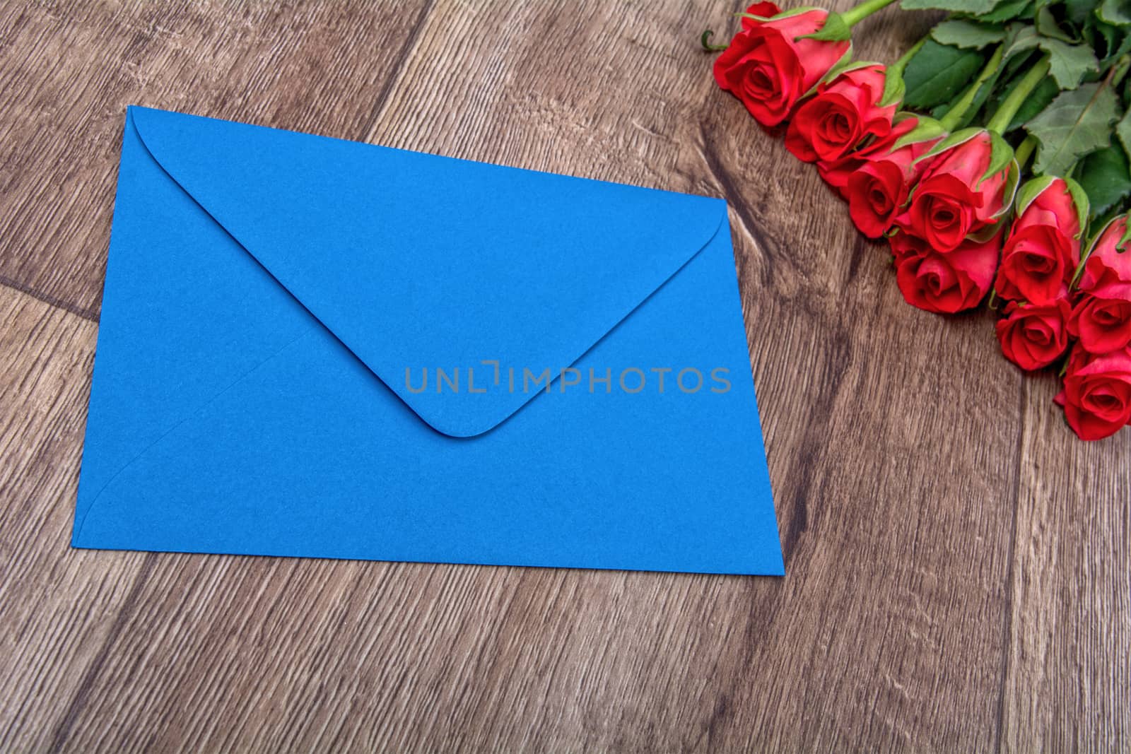 Blue envelope and red roses on a wooden background