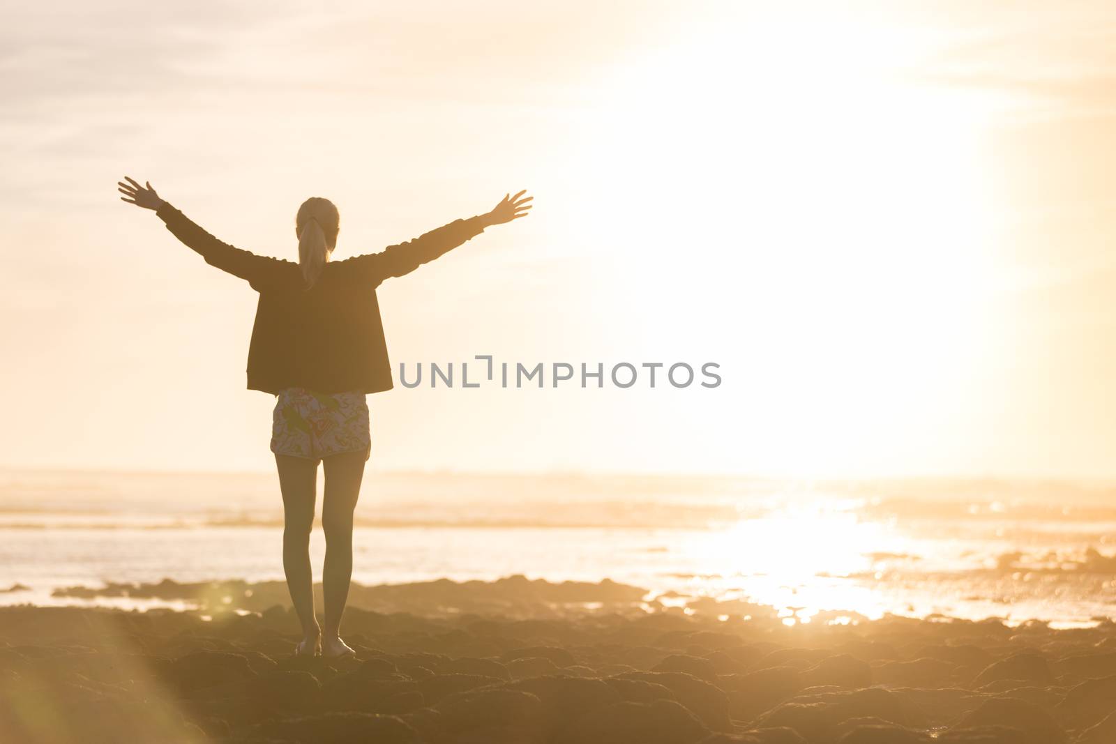 Silhouette of free woman enjoying freedom feeling happy at beach at sunset. Serene relaxing woman in pure happiness and elated enjoyment with arms raised outstretched up. 