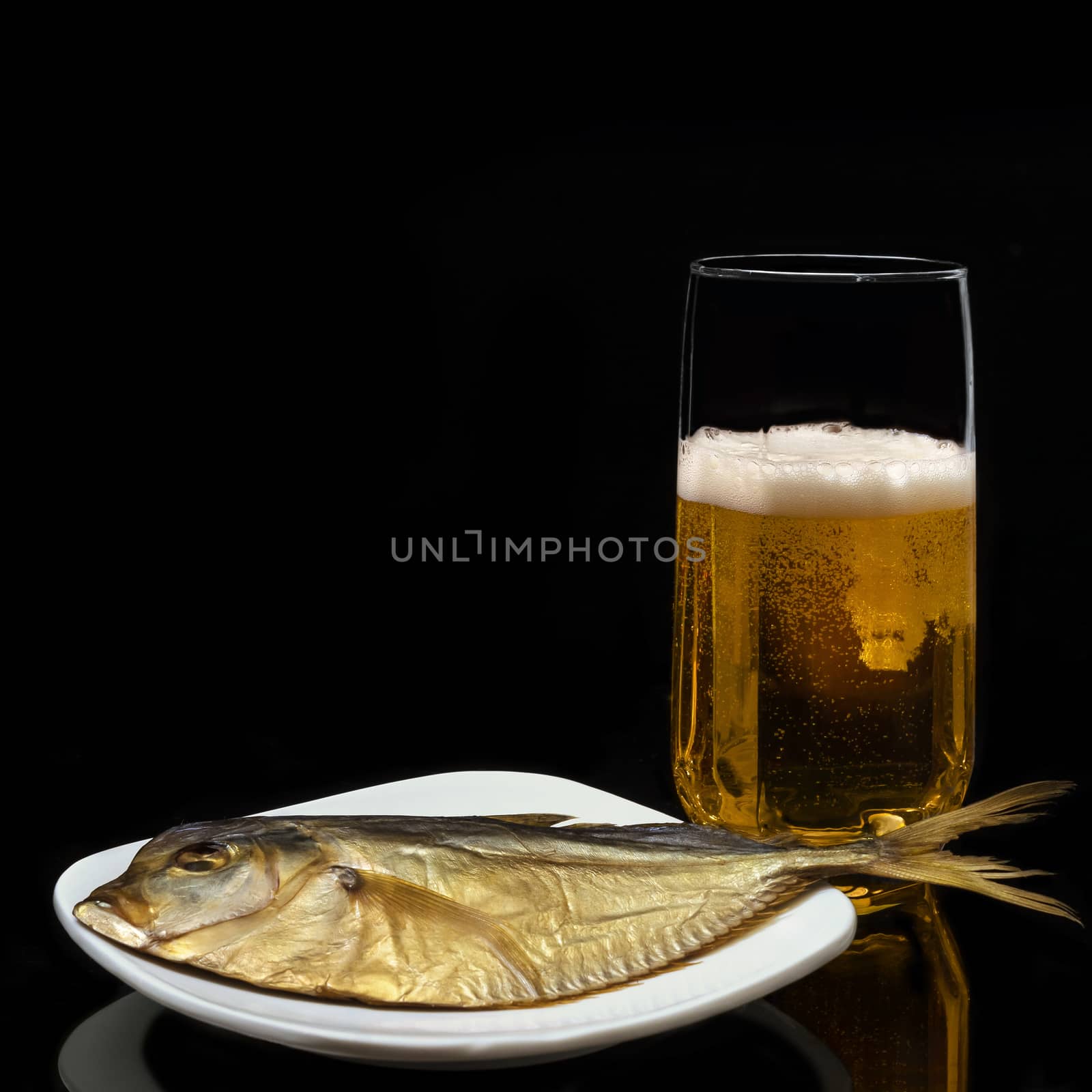 Beer in the glass and fish on a plate, on a black background