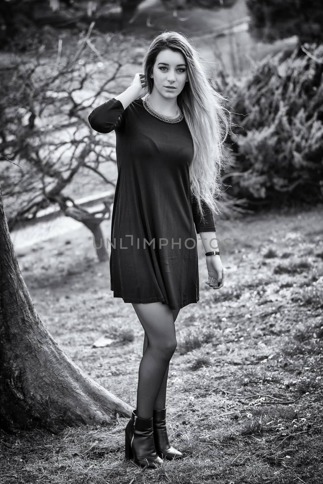 Pretty blonde young woman outdoor in city park, wearing short black dress