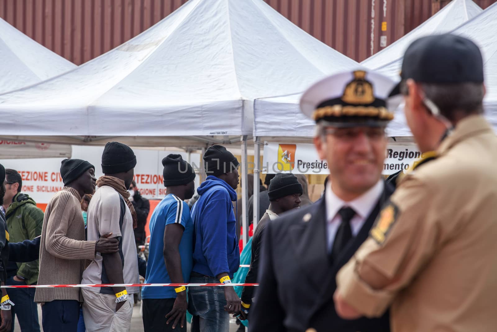 ITALY, Palermo: Officials speak to each other, as migrants line up after getting off a ship in Palermo, Italy on March 19, 2016.712 migrants have arrived at the port of Palermo, on the military Norwegian ship Siem Pilot on March 19, 2016. Among them 598 men, 51 women, and 63 children came from 30 different nationalities including Nigeria, Senegal, Guinea, Sierra Leone and other Sub-saharan countries.