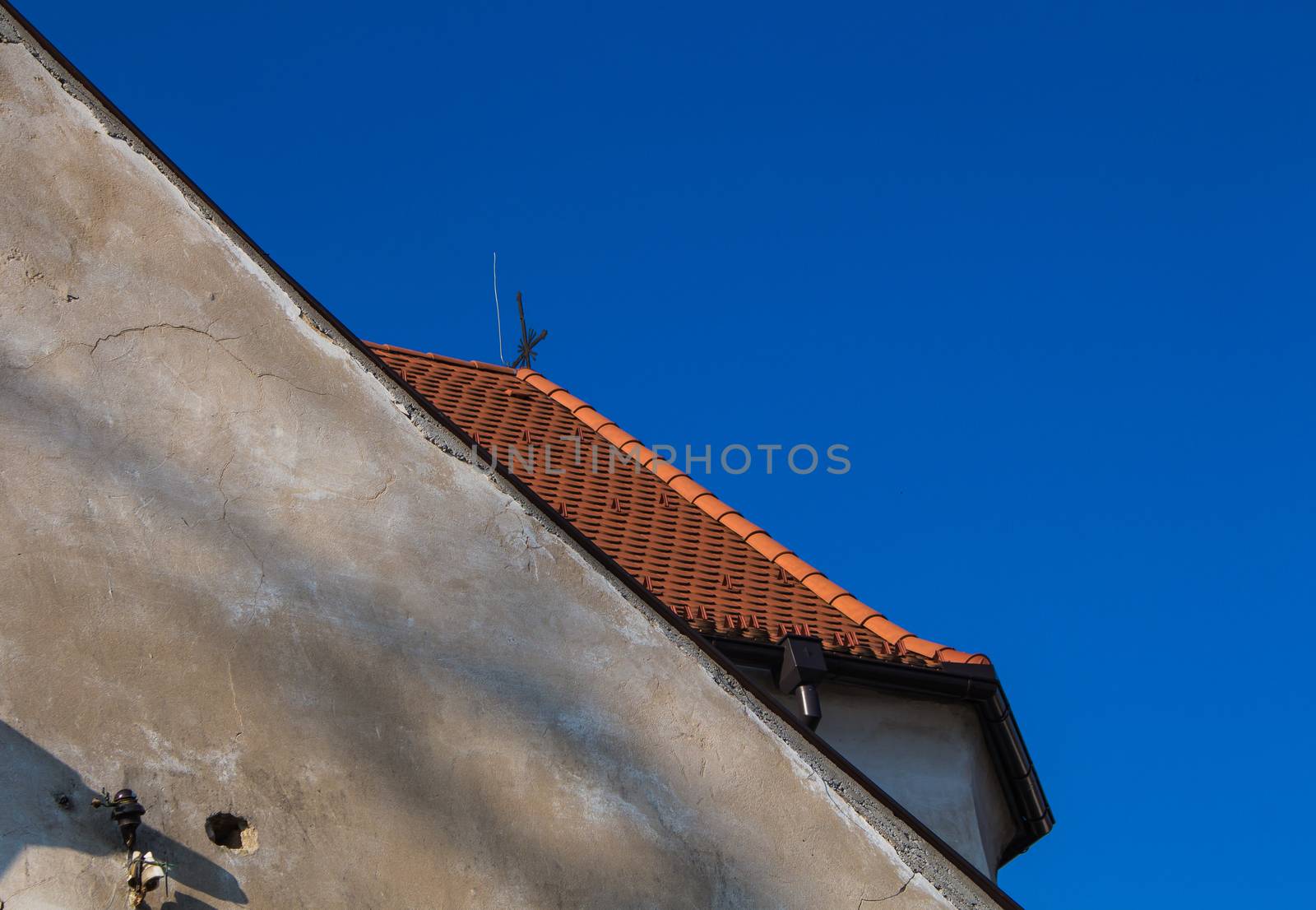 Old facade with shadows and enlightened new orange roof behind. Bright blue sky.