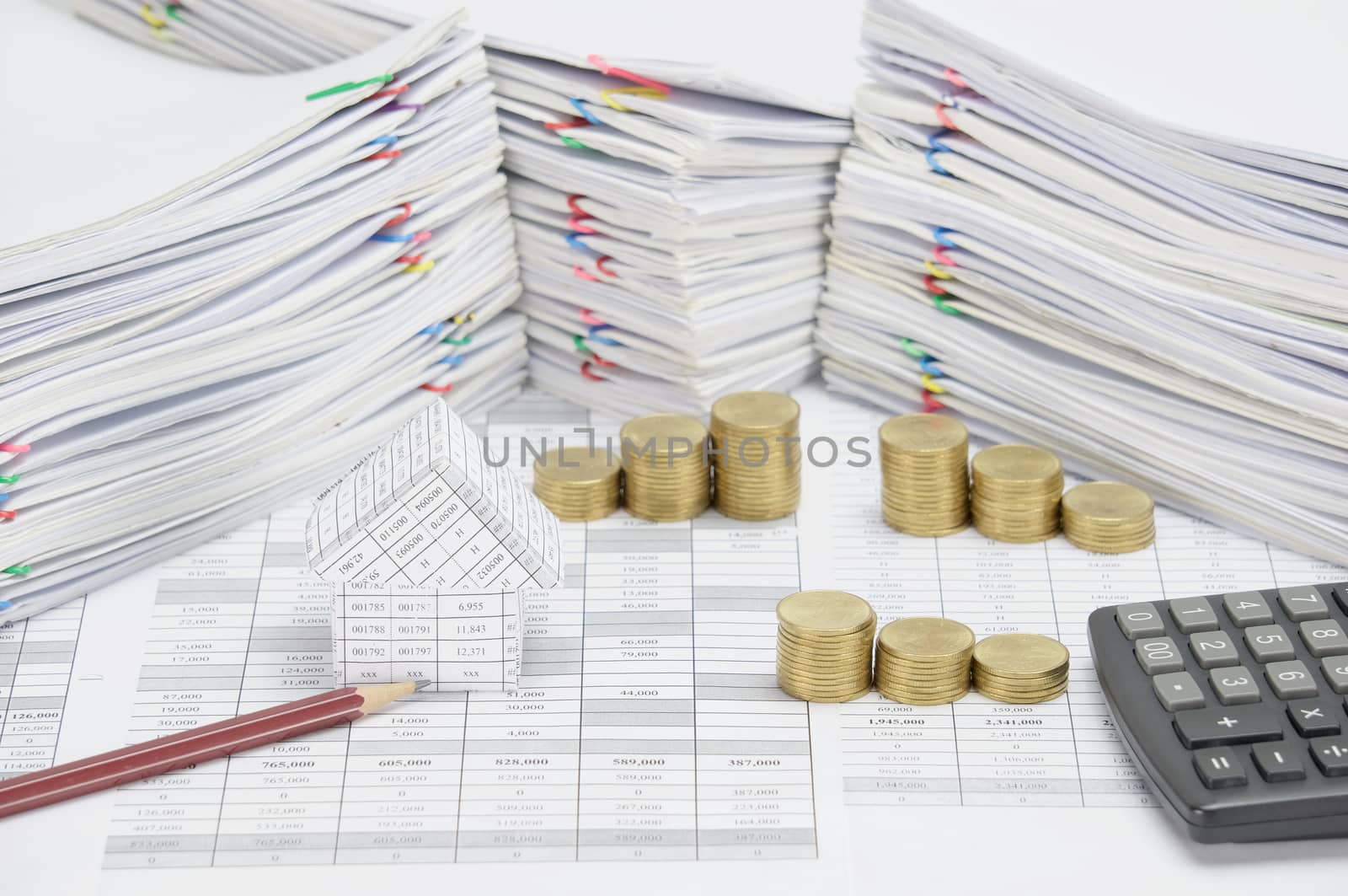 House and brown pencil on finance account have step pile of gold coins and calculator with overload of paperwork with colorful paperclip as background.