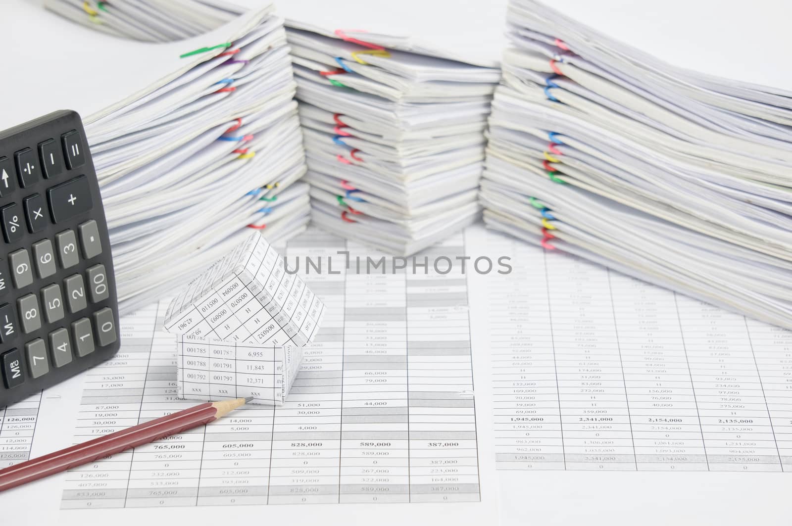 House and brown pencil on finance account have calculator place vertical with overload of paperwork with colorful paperclip as background.