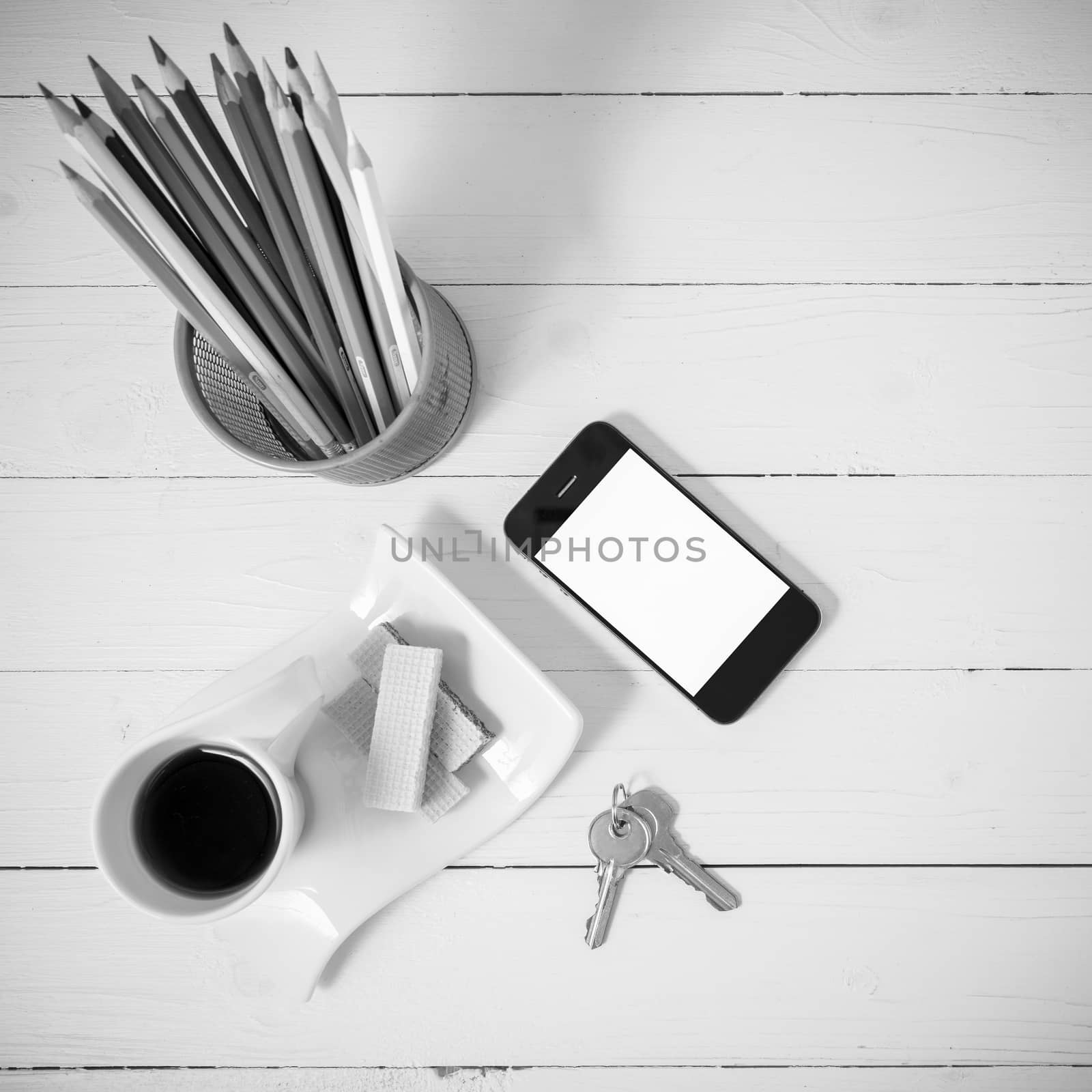 coffee cup with wafer,phone,pencil box,key on white wood background black and white color