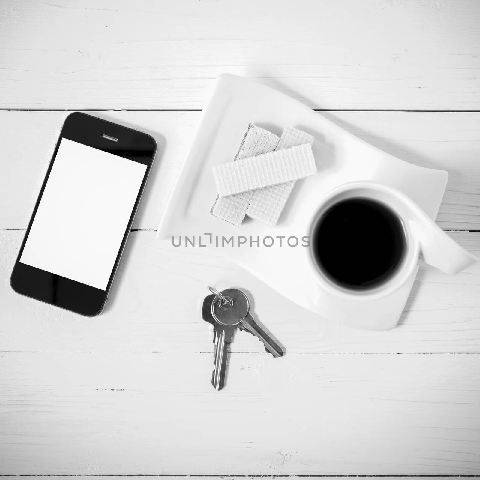 coffee cup with wafer,phone,key on white wood background black and white color