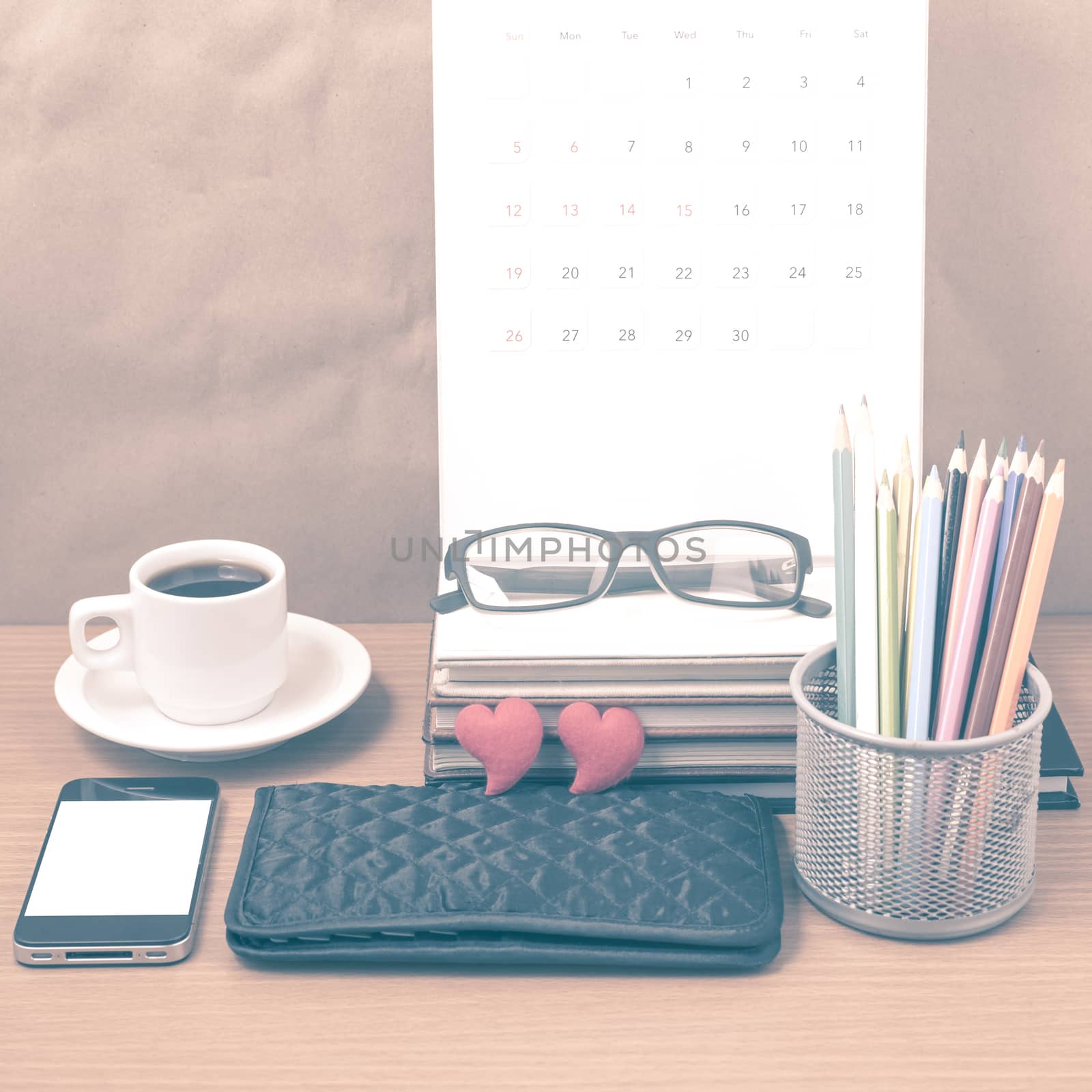 office desk : coffee with phone,wallet,calendar,color pencil box,stack of book,heart,eyeglasses on wood background vintage style