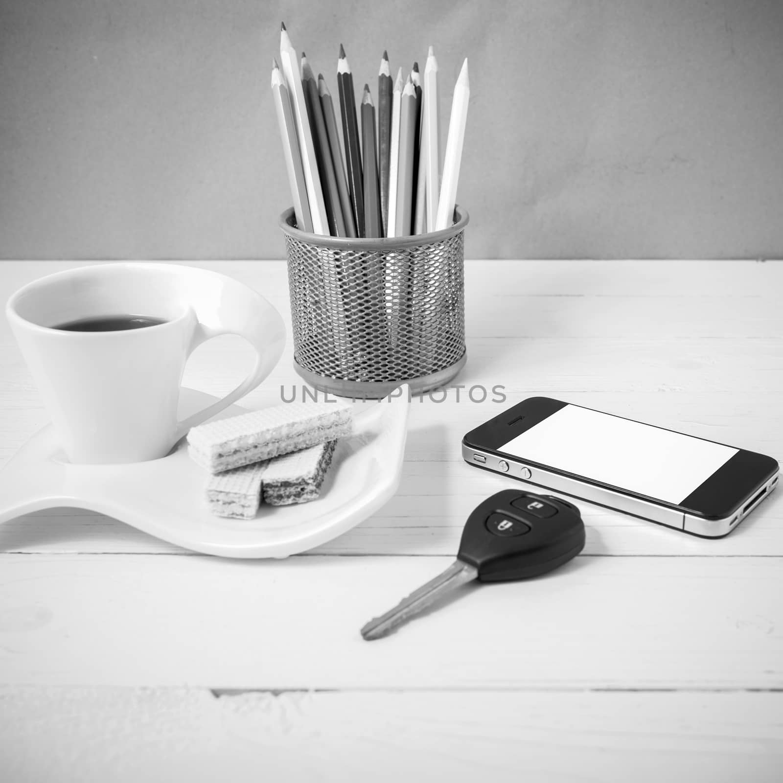 coffee cup with wafer,phone,pencil box,car key on white wood background black and white color