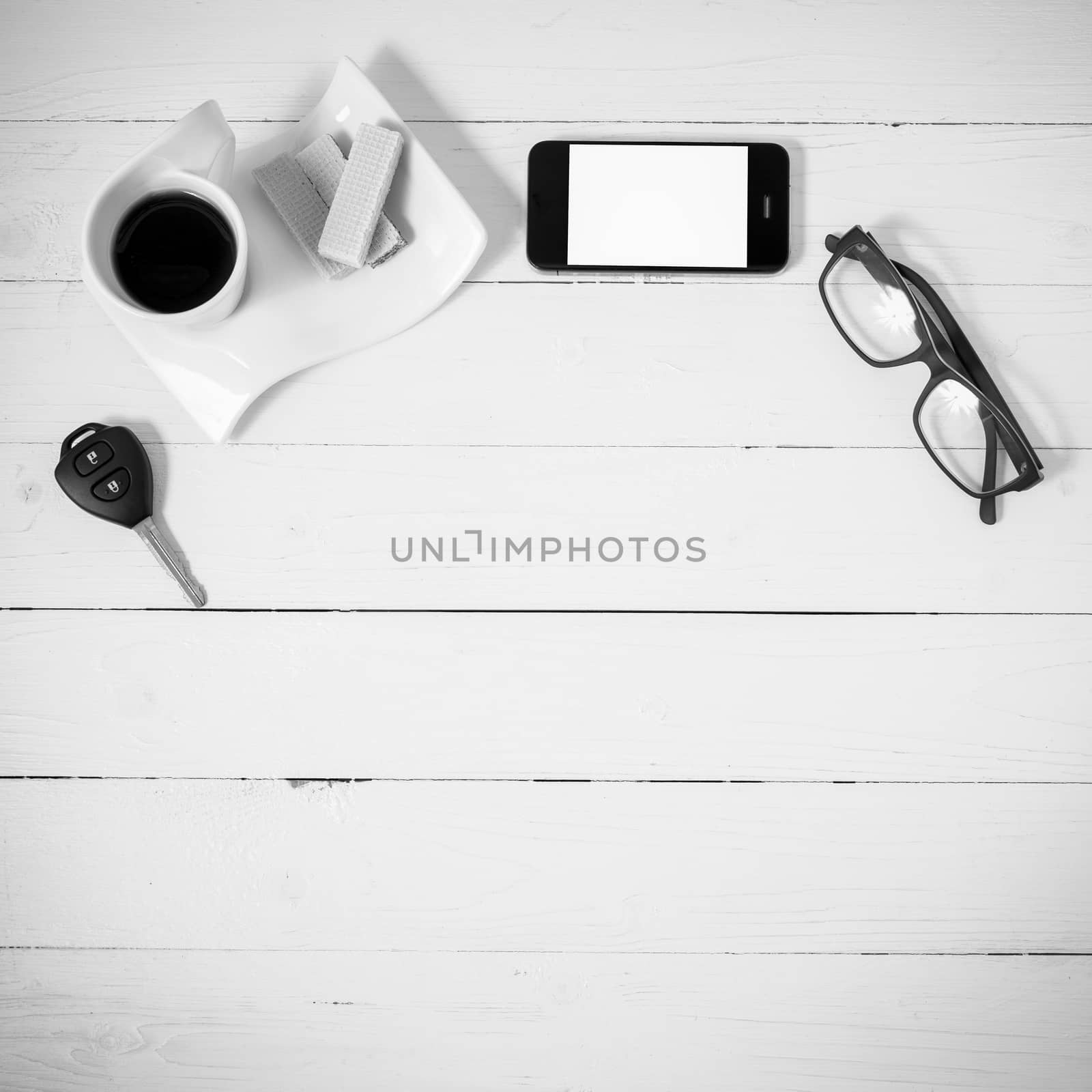 coffee cup with wafer,phone,car key,eyeglasses on white wood background black and white color