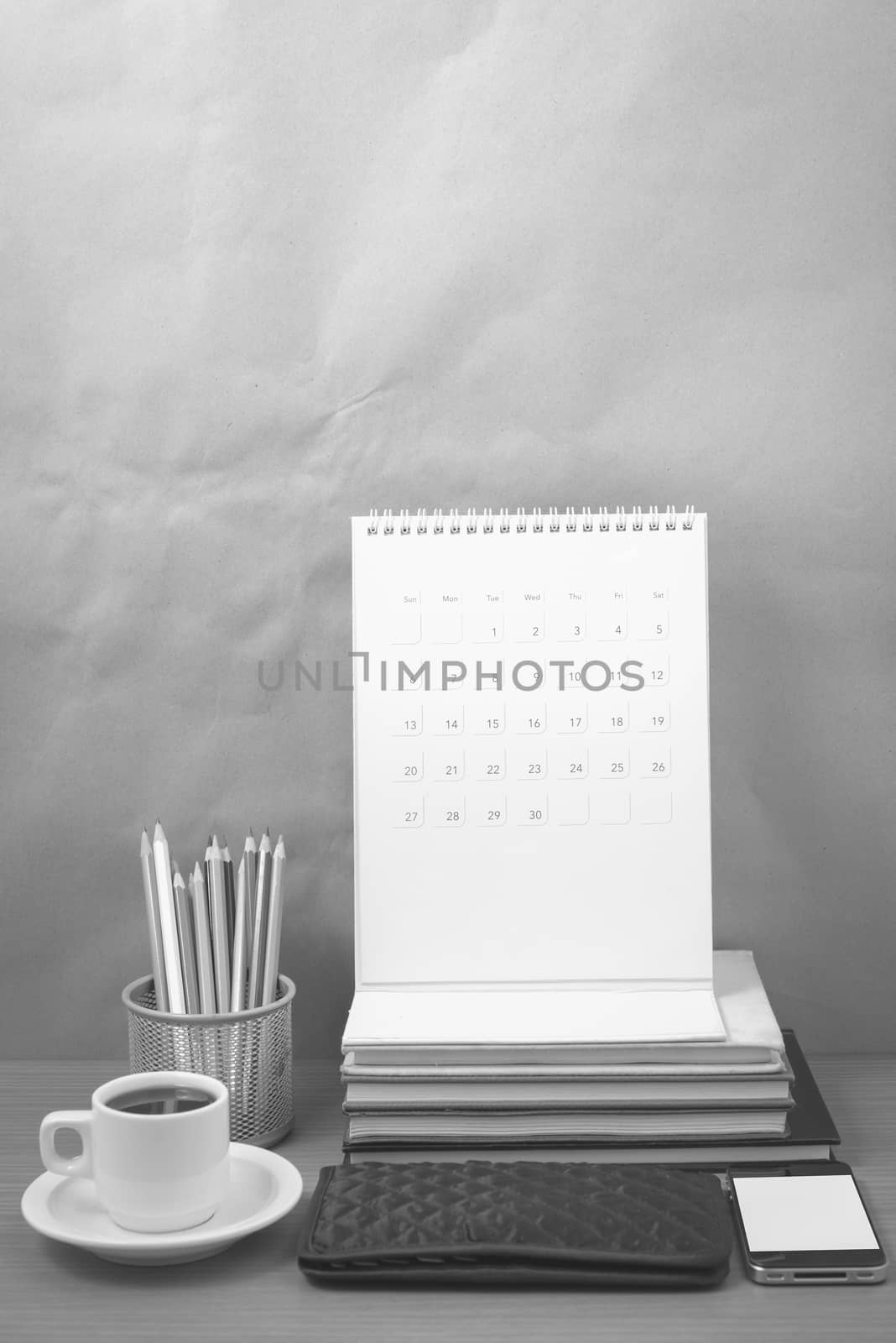 office desk : coffee with phone,wallet,calendar,color pencil box,stack of book on wood background black and white color