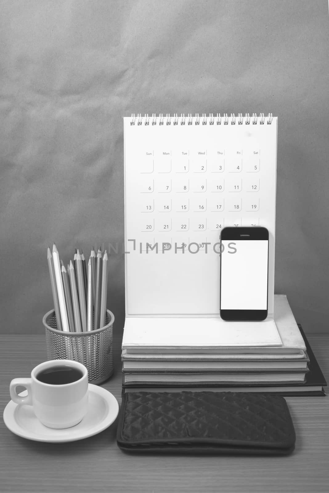 office desk : coffee with phone,wallet,calendar,color pencil box,stack of book on wood background black and white color