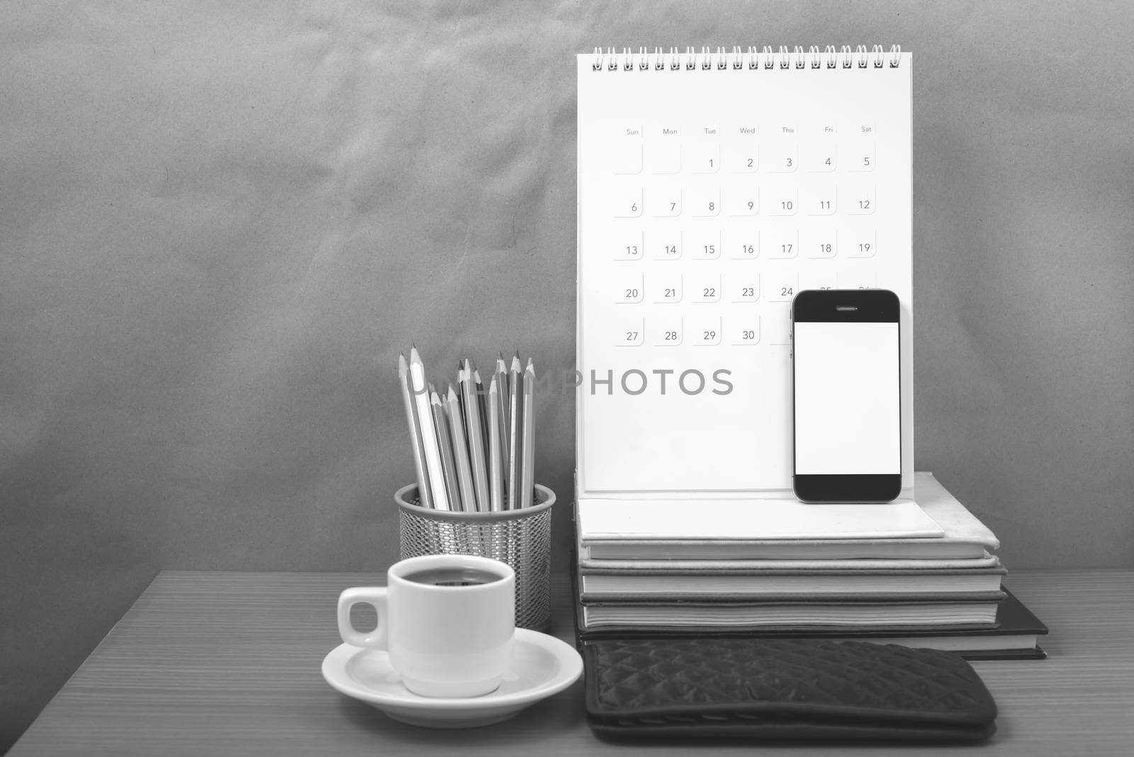 office desk : coffee with phone,wallet,calendar,color pencil box,stack of book on wood background black and white color