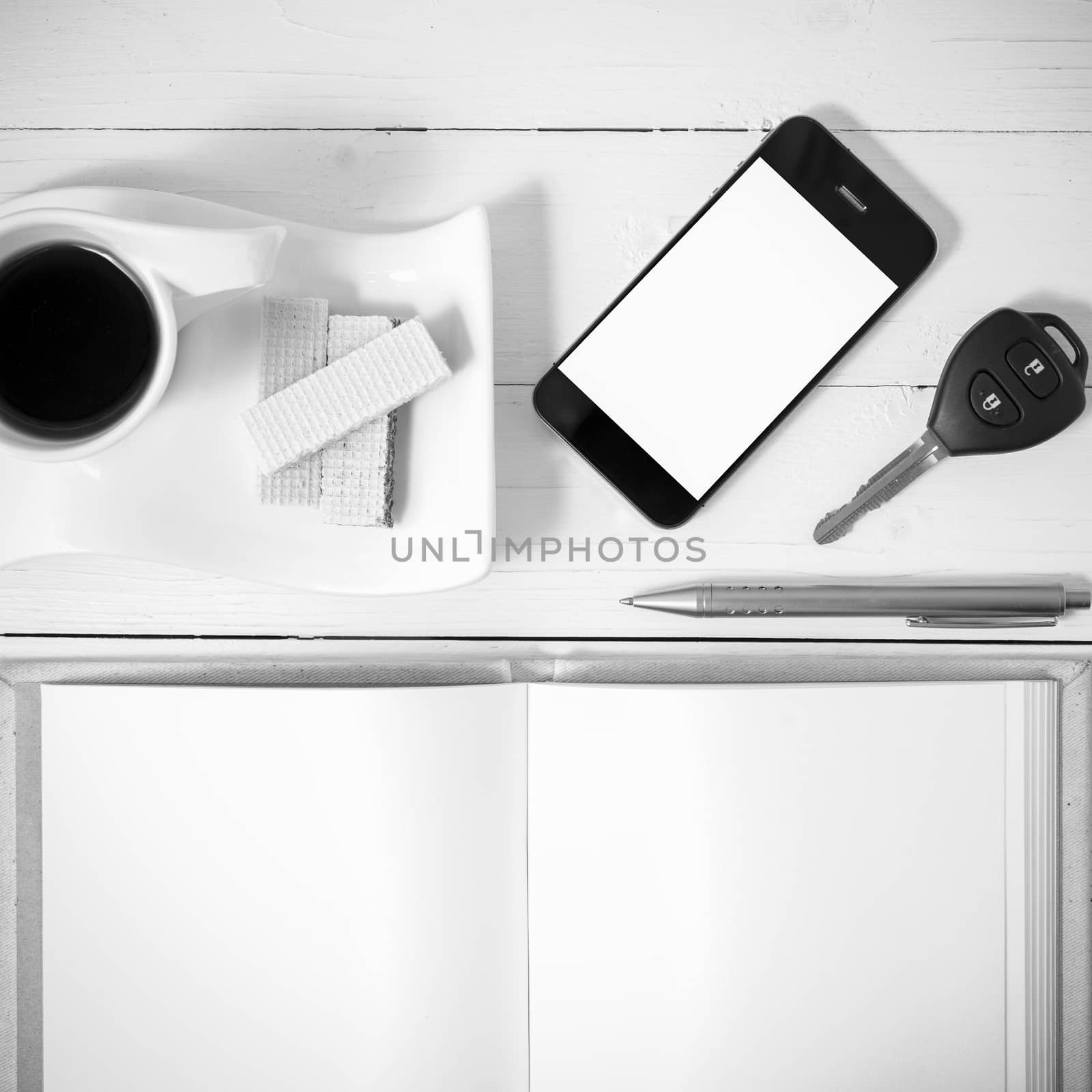 coffee cup with wafer,phone,car key,notebook on white wood background black and white color