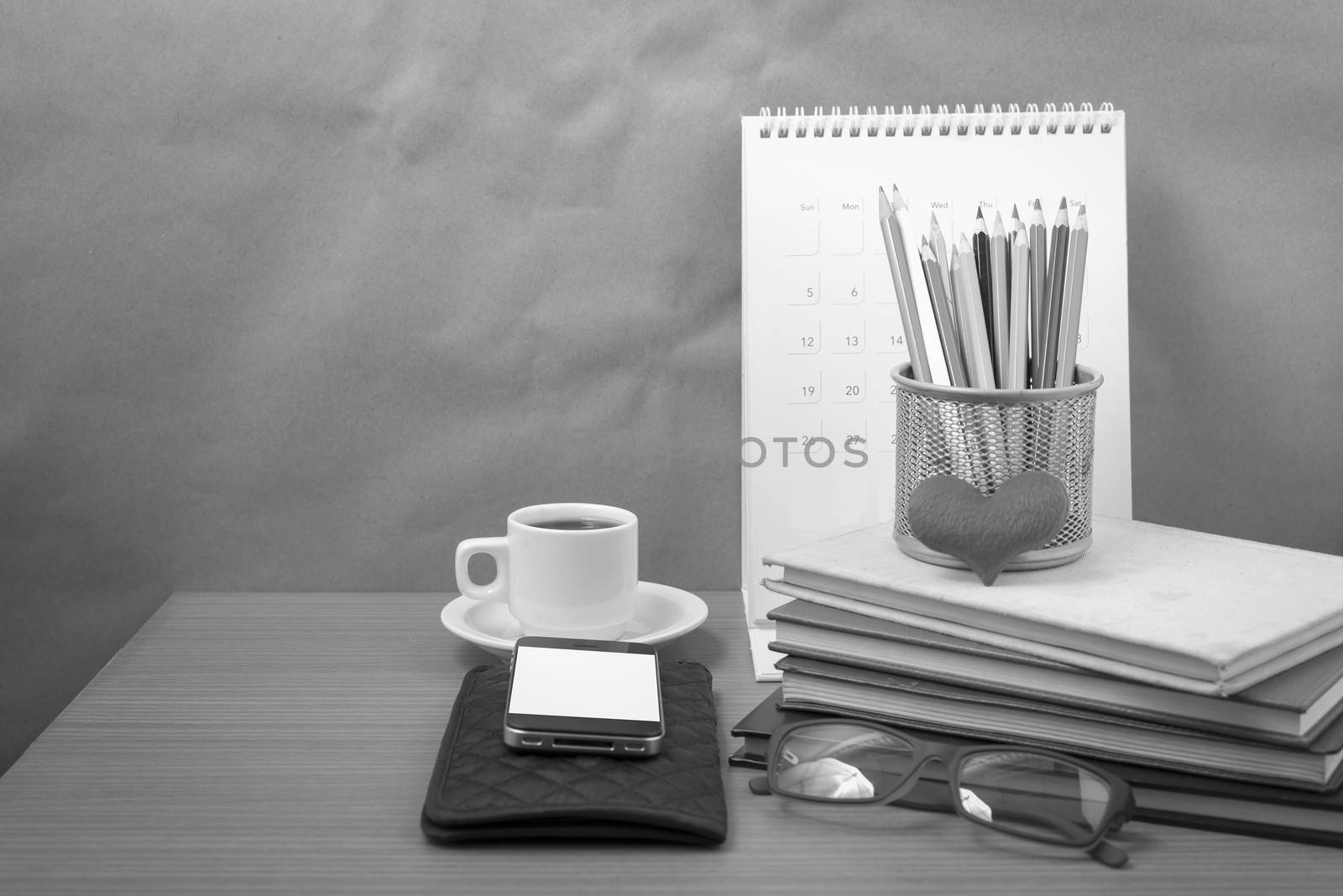 office desk : coffee with phone,wallet,calendar,color pencil box,stack of book,heart,eyeglasses on wood background black and white color