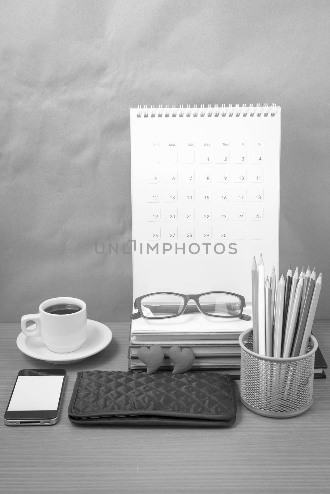office desk : coffee with phone,wallet,calendar,color pencil box,stack of book,heart,eyeglasses on wood background black and white color