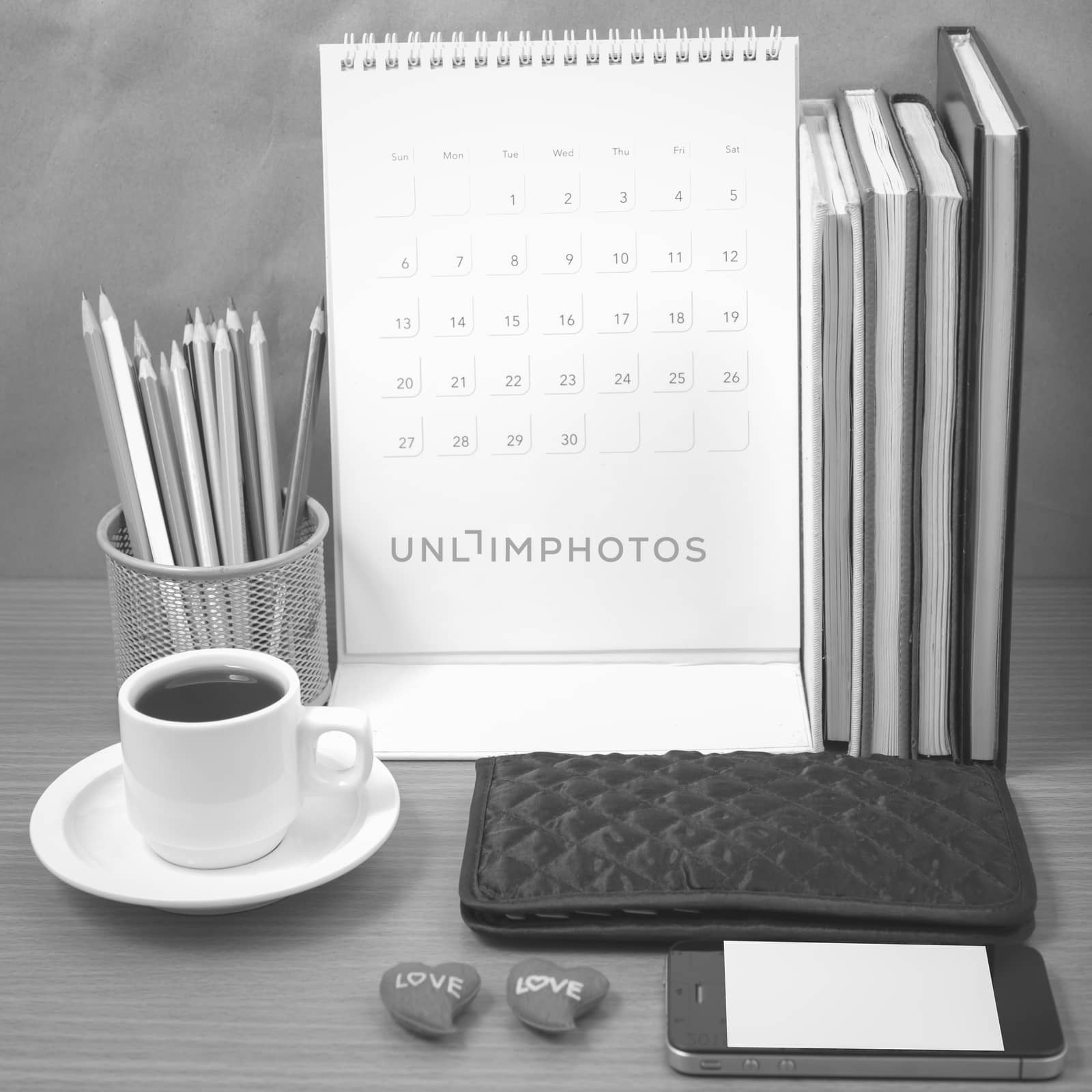 office desk : coffee with phone,wallet,calendar,heart,color pencil box,stack of book,heart on wood background black and white color