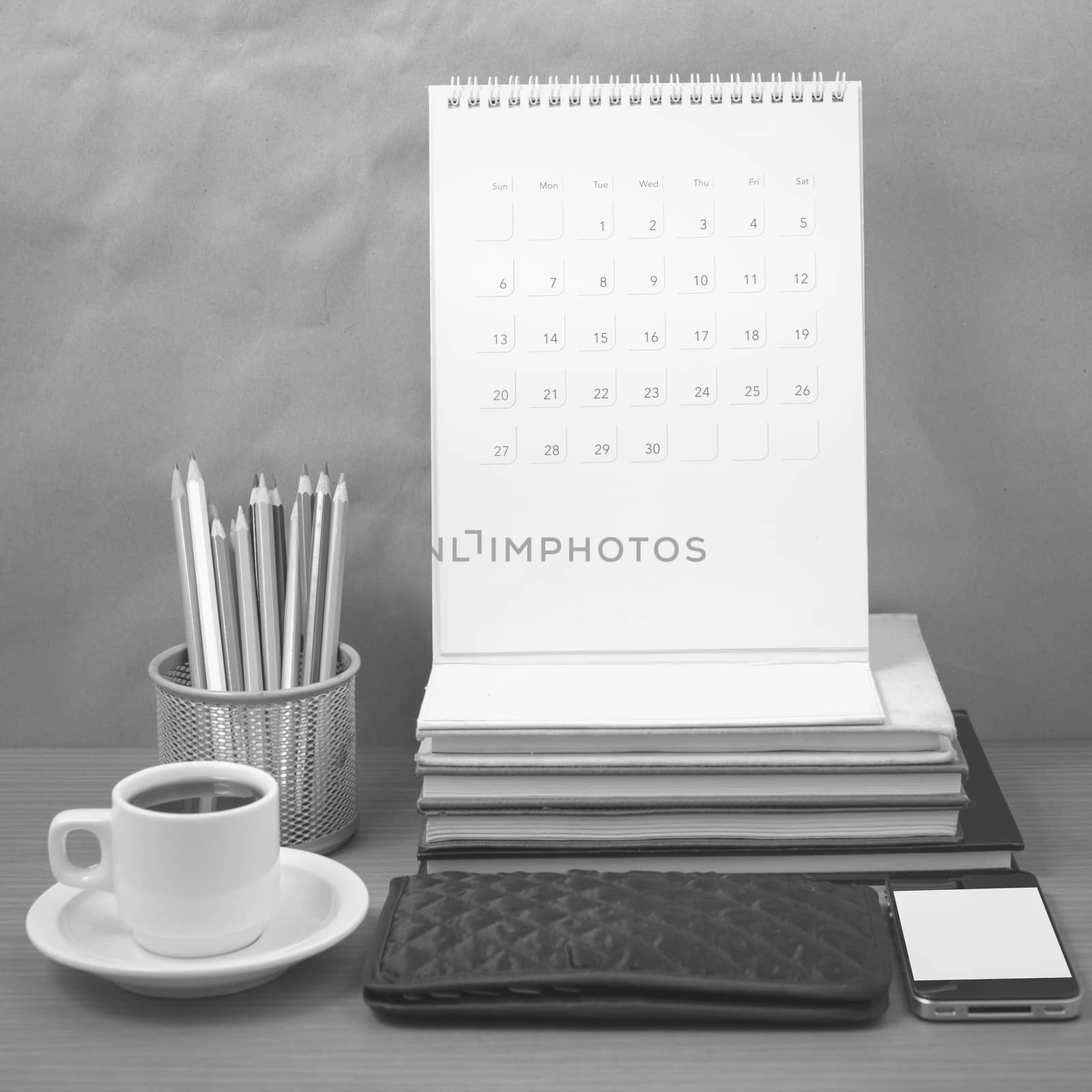 office desk : coffee with phone,wallet,calendar,color pencil box,stack of book on wood background black and white color