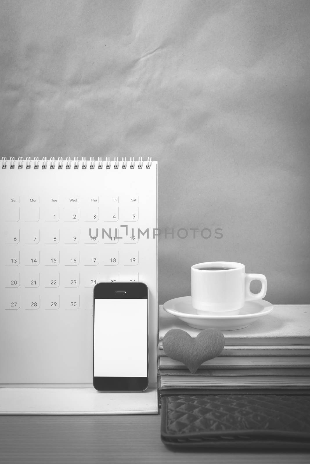 office desk : coffee with phone,wallet,calendar,heart,stack of book on wood background black and white color