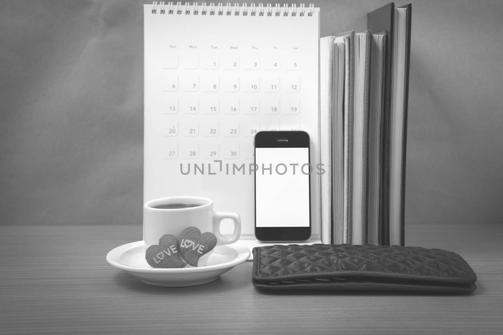 office desk : coffee with phone,wallet,calendar,heart,stack of book on wood background black and white color