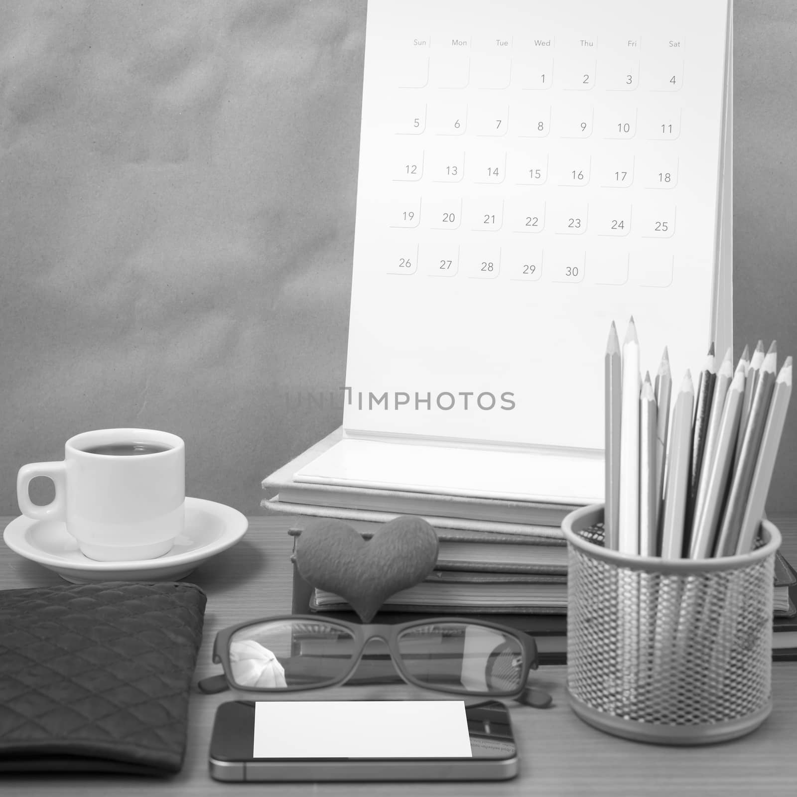 office desk : coffee with phone,wallet,calendar,color pencil box,stack of book,heart,eyeglasses on wood background black and white color