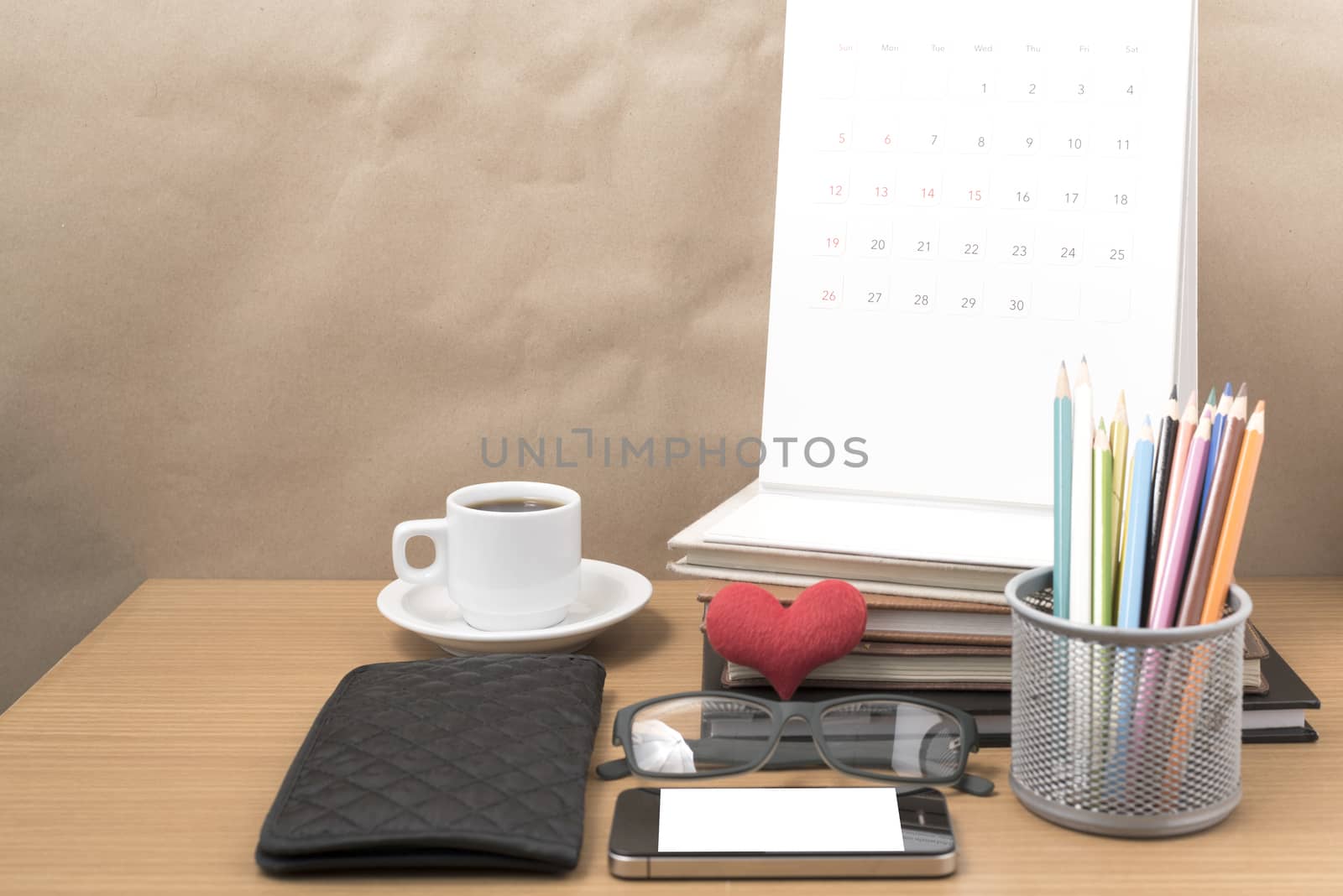 office desk : coffee with phone,wallet,calendar,color pencil box,stack of book,heart,eyeglasses on wood background