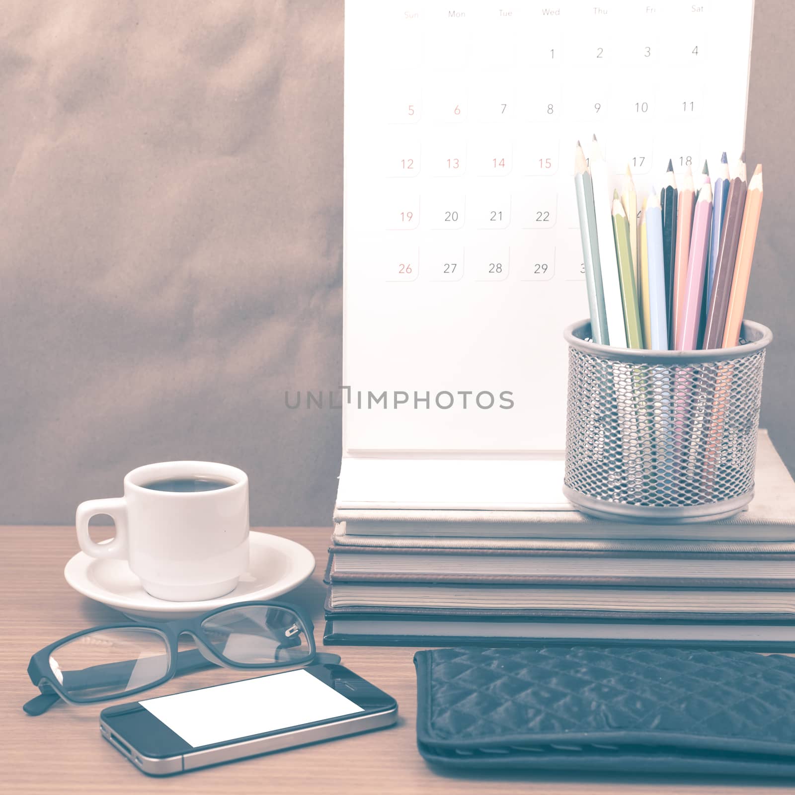 office desk : coffee with phone,wallet,calendar,color pencil box,stack of book,eyeglasses on wood background vintage style