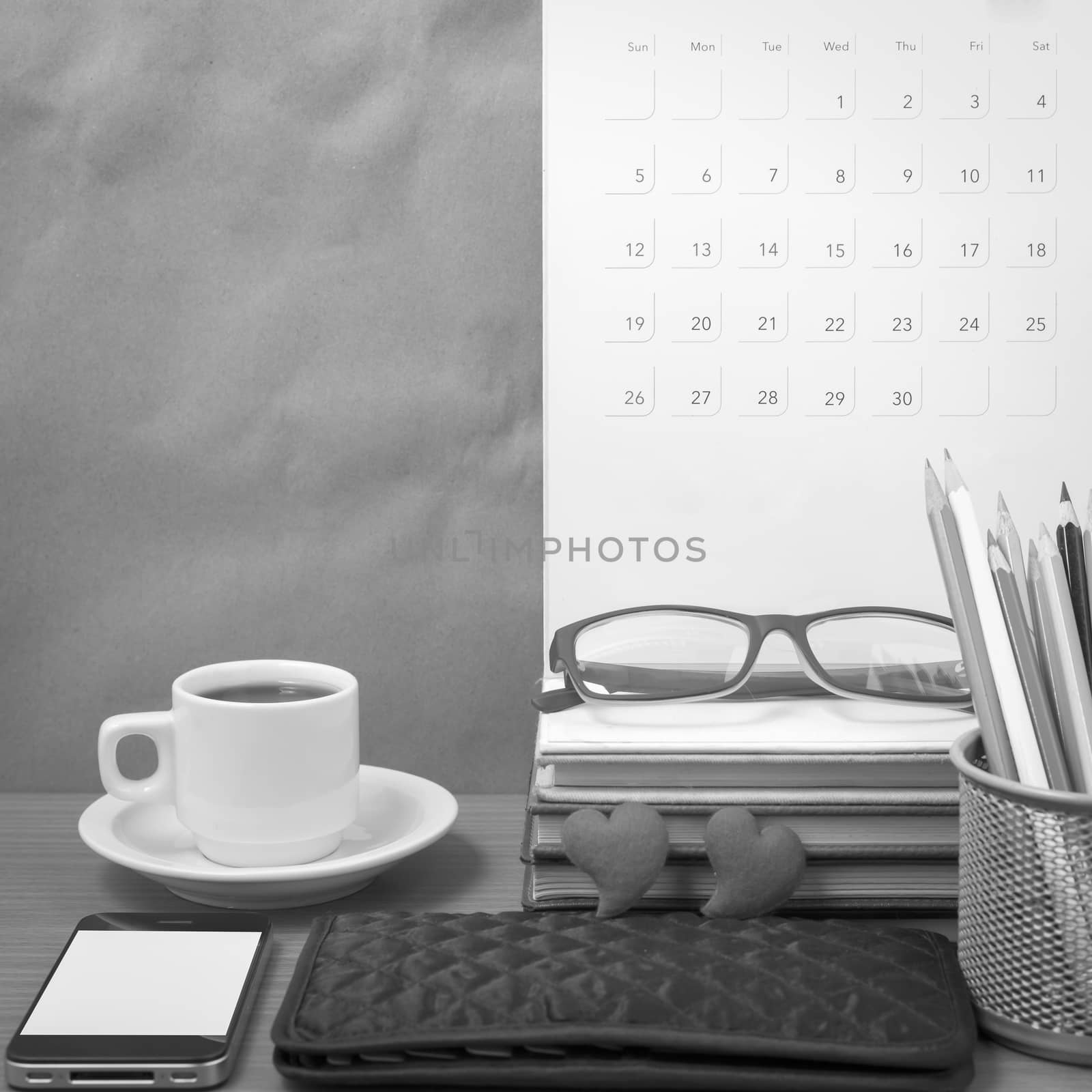 office desk : coffee with phone,wallet,calendar,color pencil box,stack of book,heart,eyeglasses on wood background black and white color