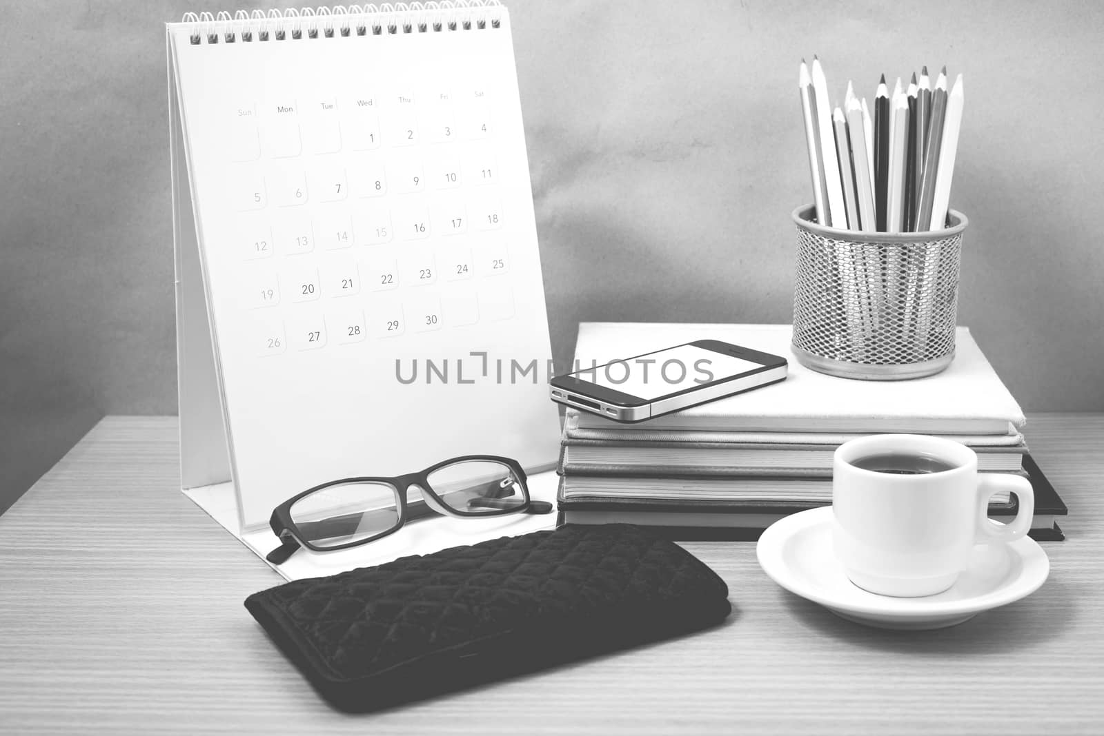 office desk : coffee with phone,wallet,calendar,color pencil box,stack of book,eyeglasses on wood background black and white color