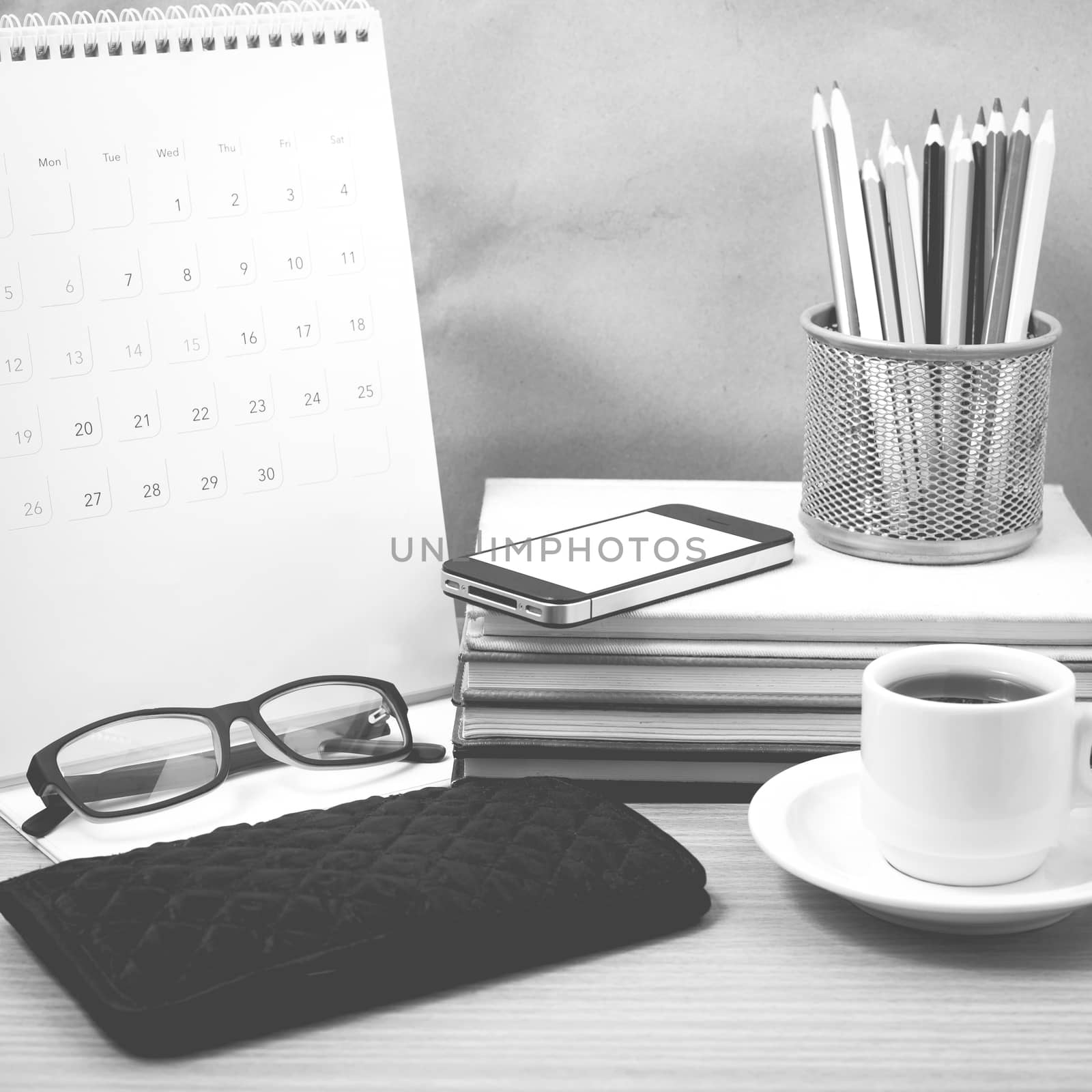 office desk : coffee with phone,wallet,calendar,color pencil box,stack of book,eyeglasses on wood background black and white color