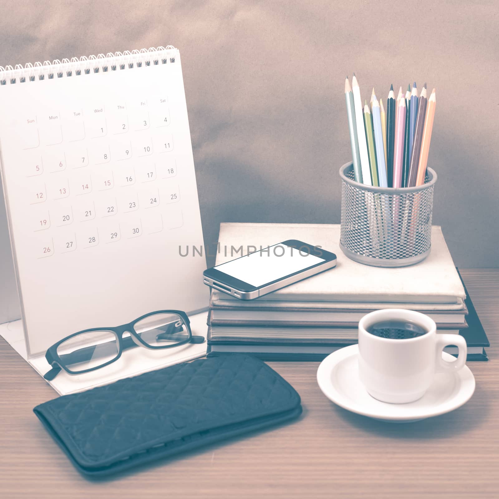 office desk : coffee with phone,wallet,calendar,color pencil box,stack of book,eyeglasses on wood background vintage style