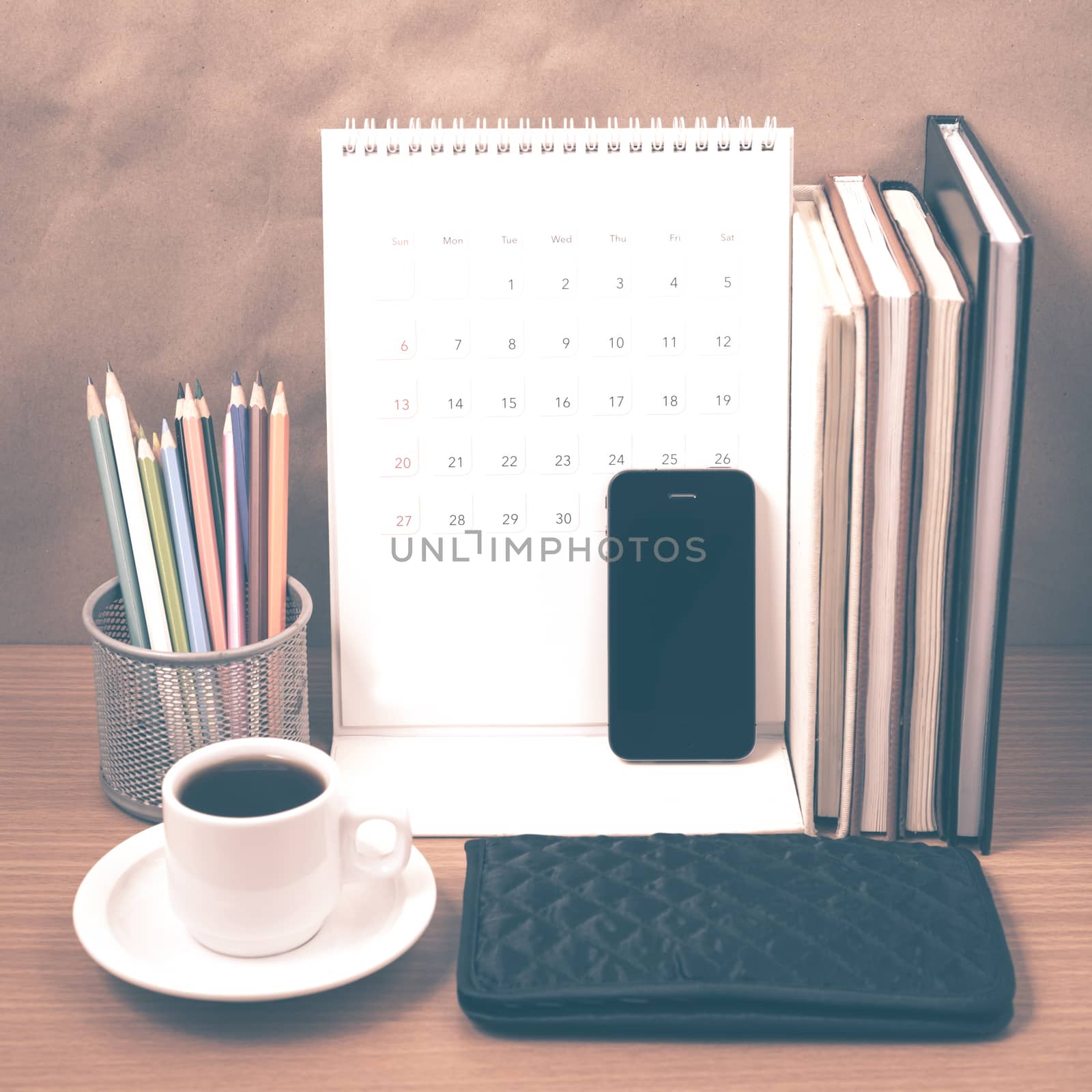 office desk : coffee with phone,wallet,calendar,color pencil box,stack of book on wood background vintage style