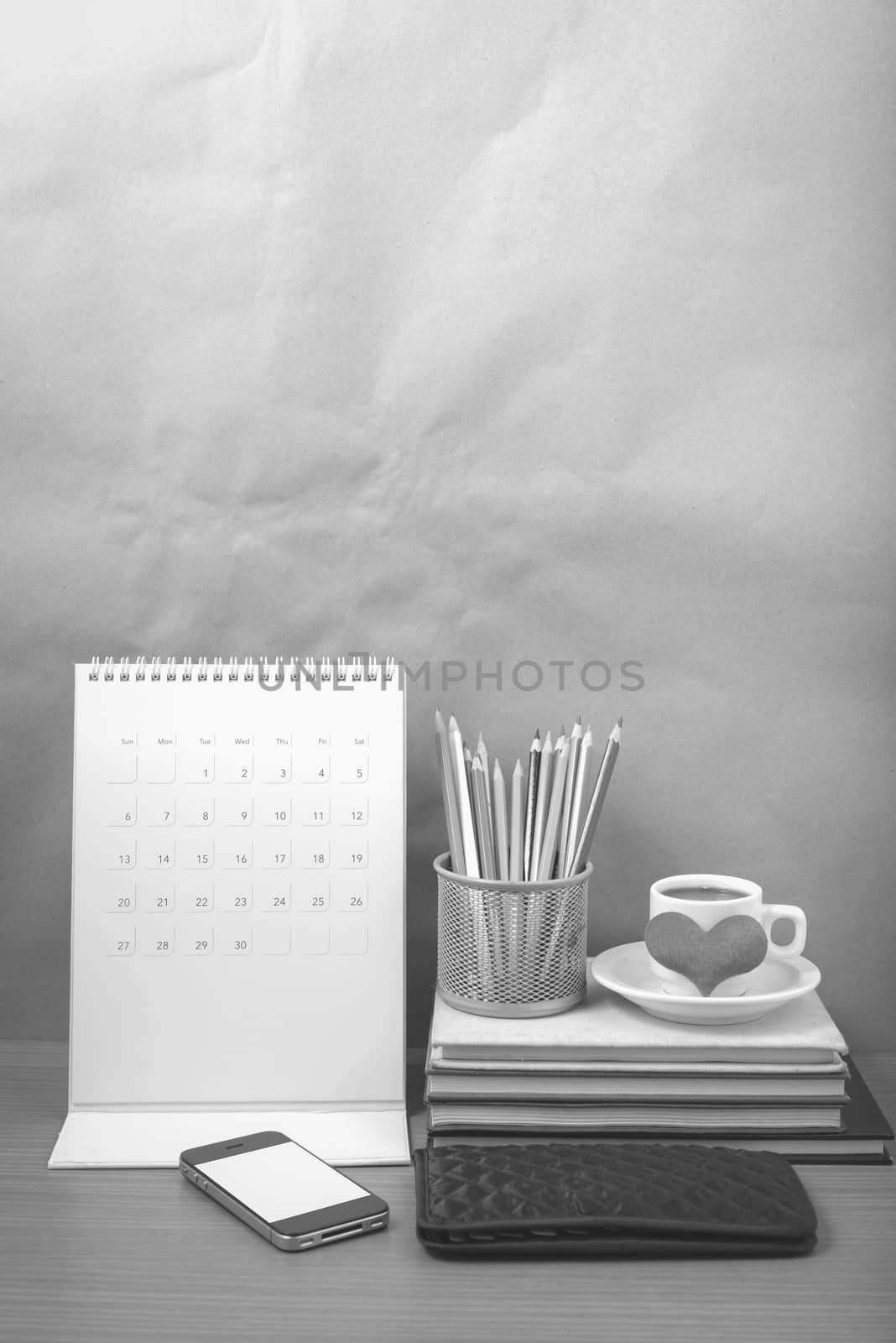 office desk : coffee with phone,wallet,calendar,heart,color pencil box,stack of book,heart on wood background black and white color