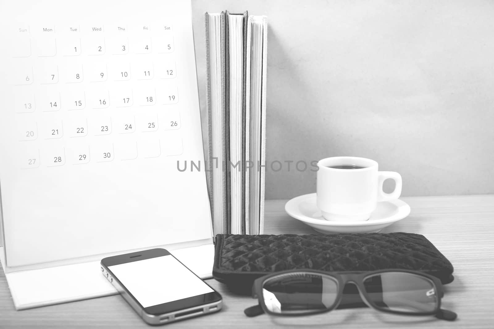 office desk : coffee with phone,stack of book,eyeglasses,wallet,calendar on wood background black and white color