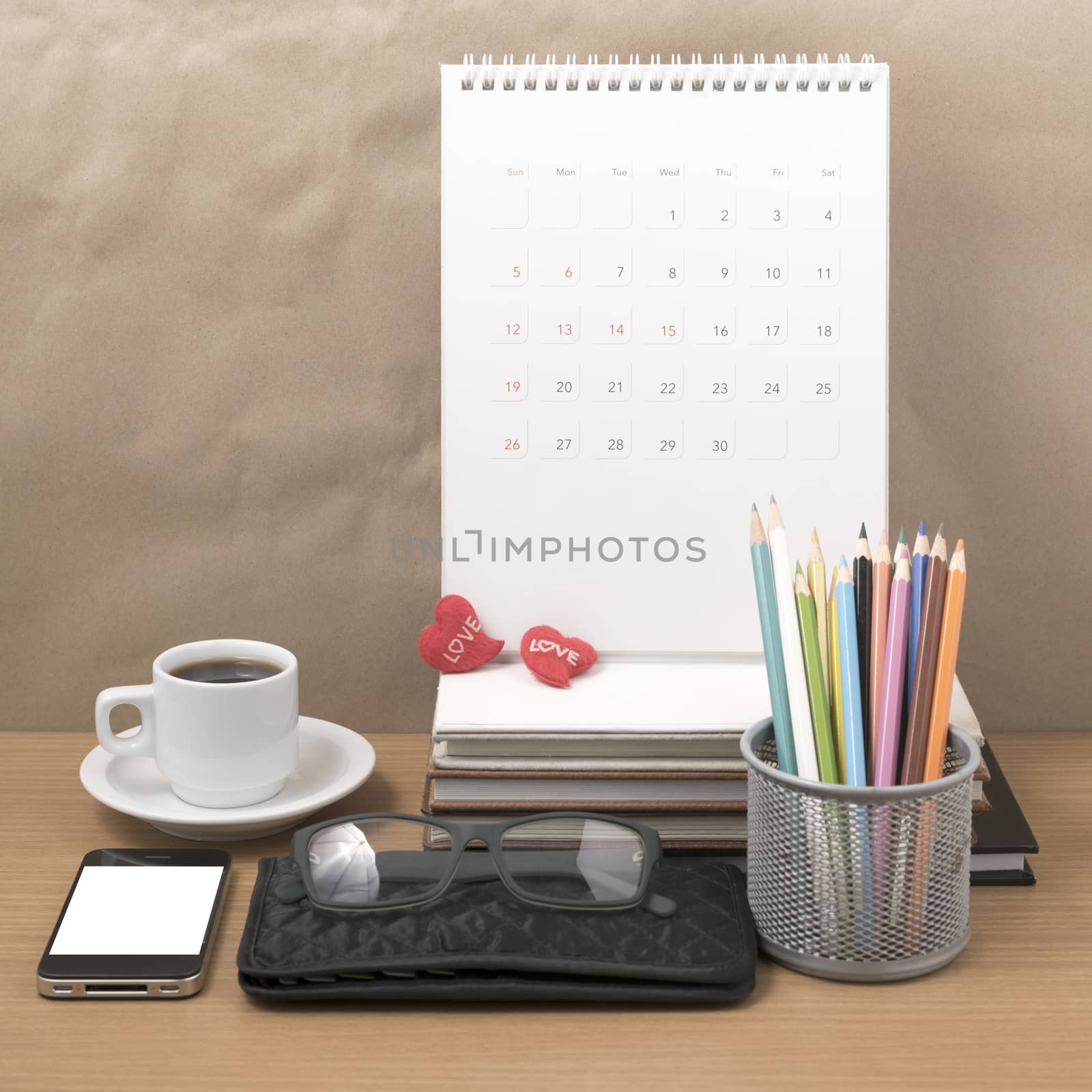 office desk : coffee with phone,wallet,calendar,color pencil box,stack of book,heart,eyeglasses on wood background