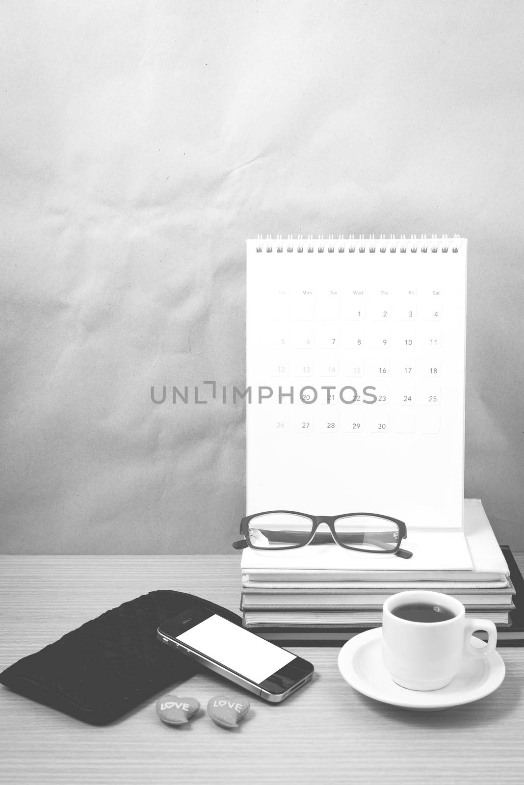 office desk : coffee with phone,wallet,calendar,heart,stack of book,eyeglasses on wood background black and white color