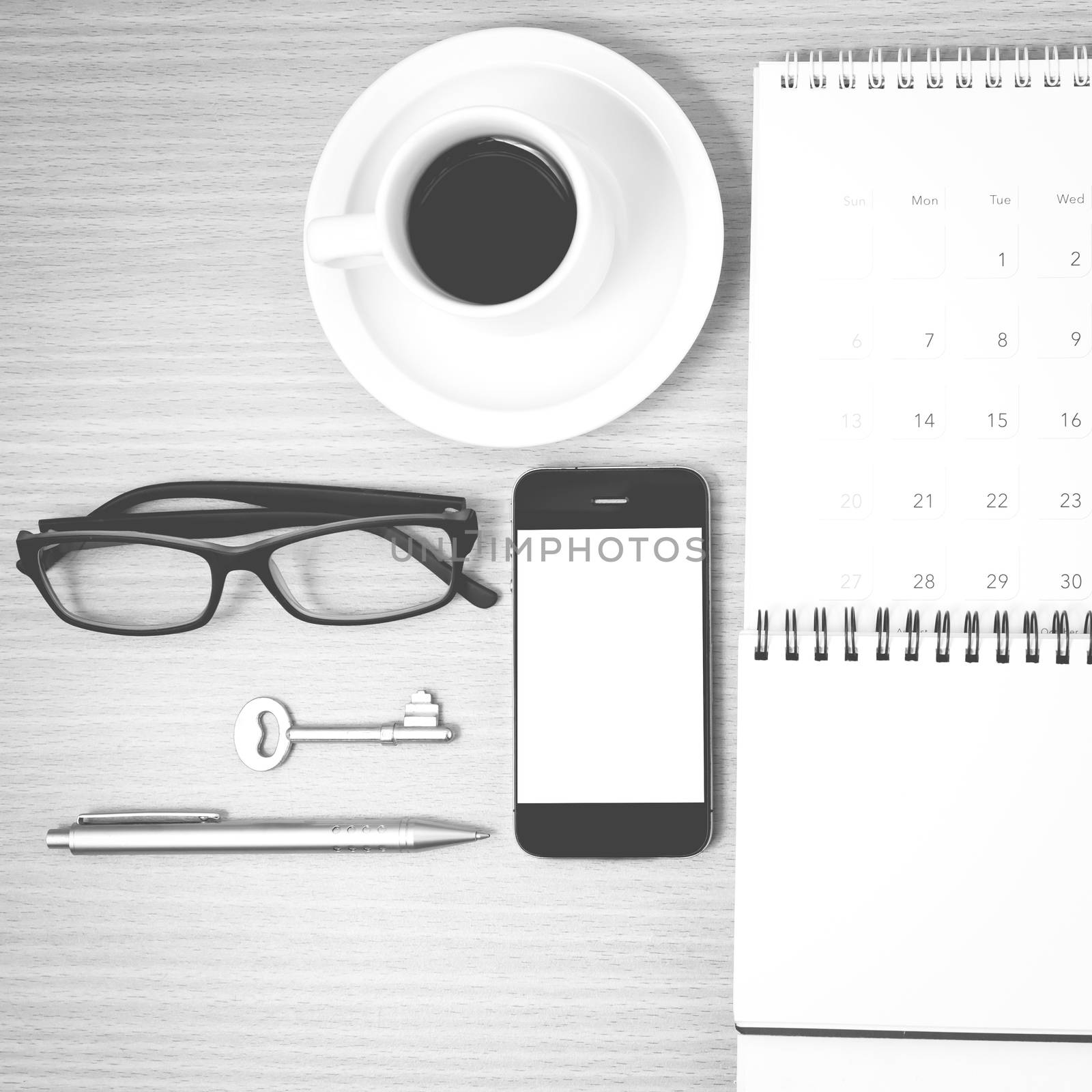 coffee and phone with key,eyeglasses,notepad,calendar on wood table background black and white color