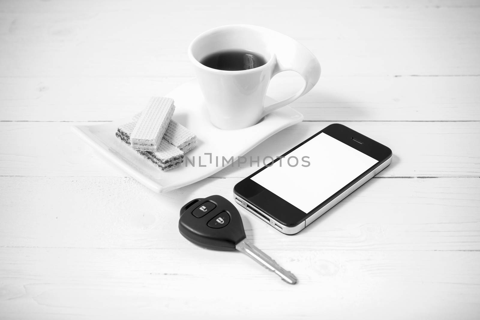 coffee cup with wafer,phone,car key on white wood background black and white color